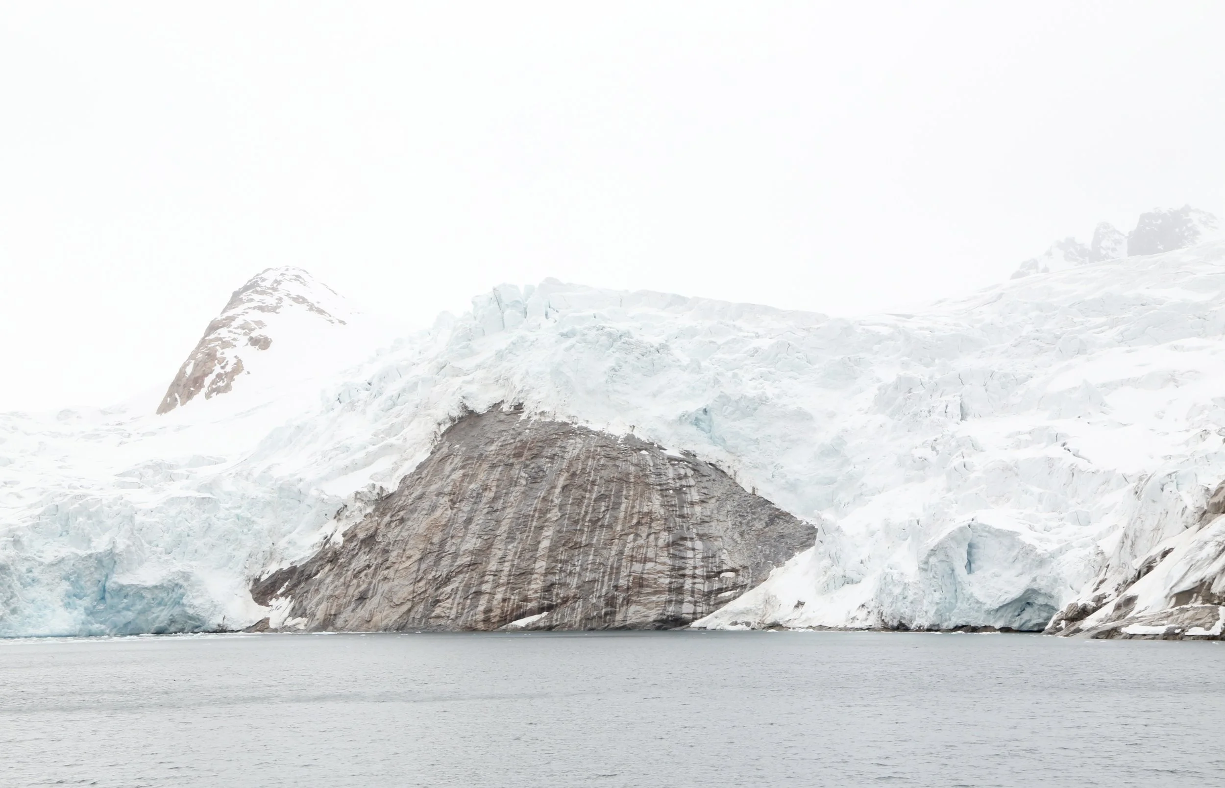 Glacier with ice and snow, partially calving into a body of water