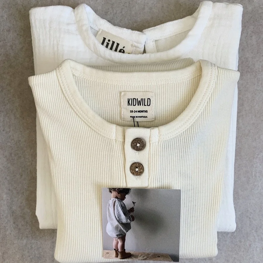 Two cream-colored children's shirts folded on top of each other, with a small photo of a child holding a flower placed on the front shirt.