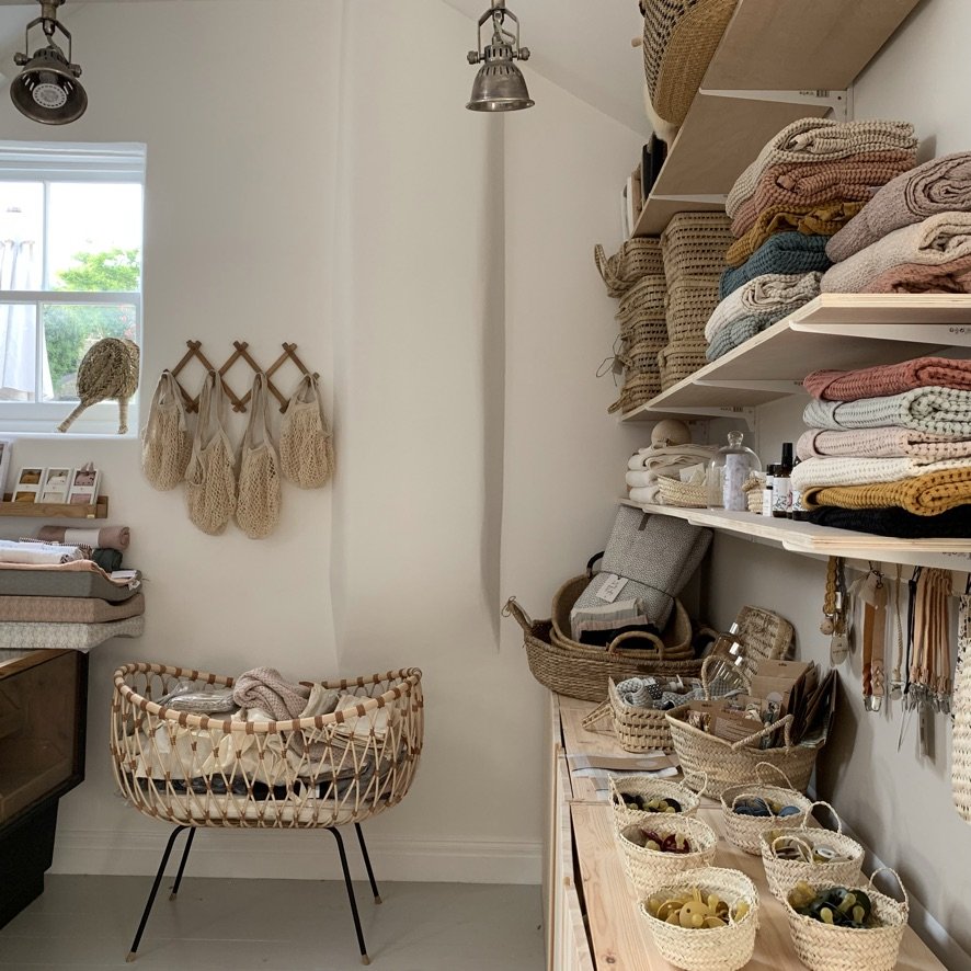 A cozy storage space with shelves holding folded towels, baskets, and skincare products. A lamp hangs from the ceiling, and a wicker crib is nearby.