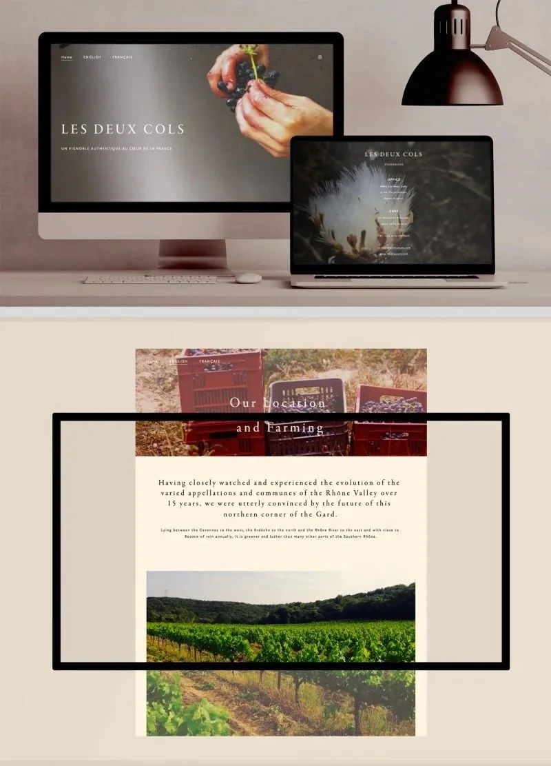 A computer and a laptop displaying websites about farming and vineyards on a desk with a black desk lamp hanging above.