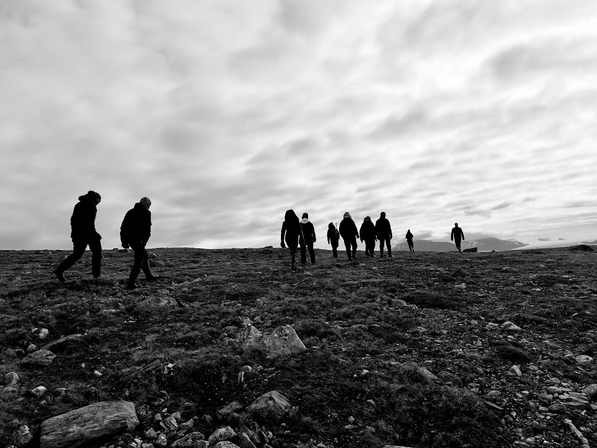Group of people hiking on a rocky landscape under cloudy sky, silhouetted against the horizon.