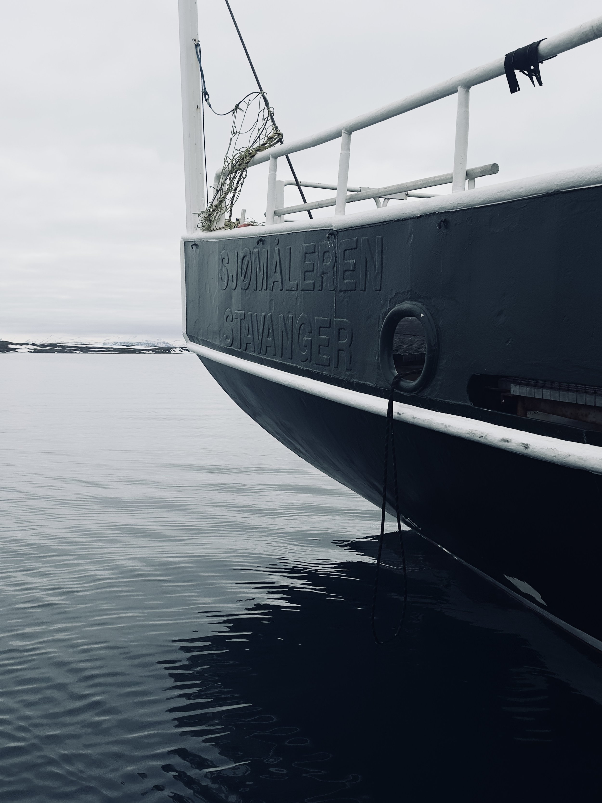 Close-up of the bow of a boat with the name 'Sjømaleren Stjånger' on the side, floating on calm water in a cold, cloudy environment.