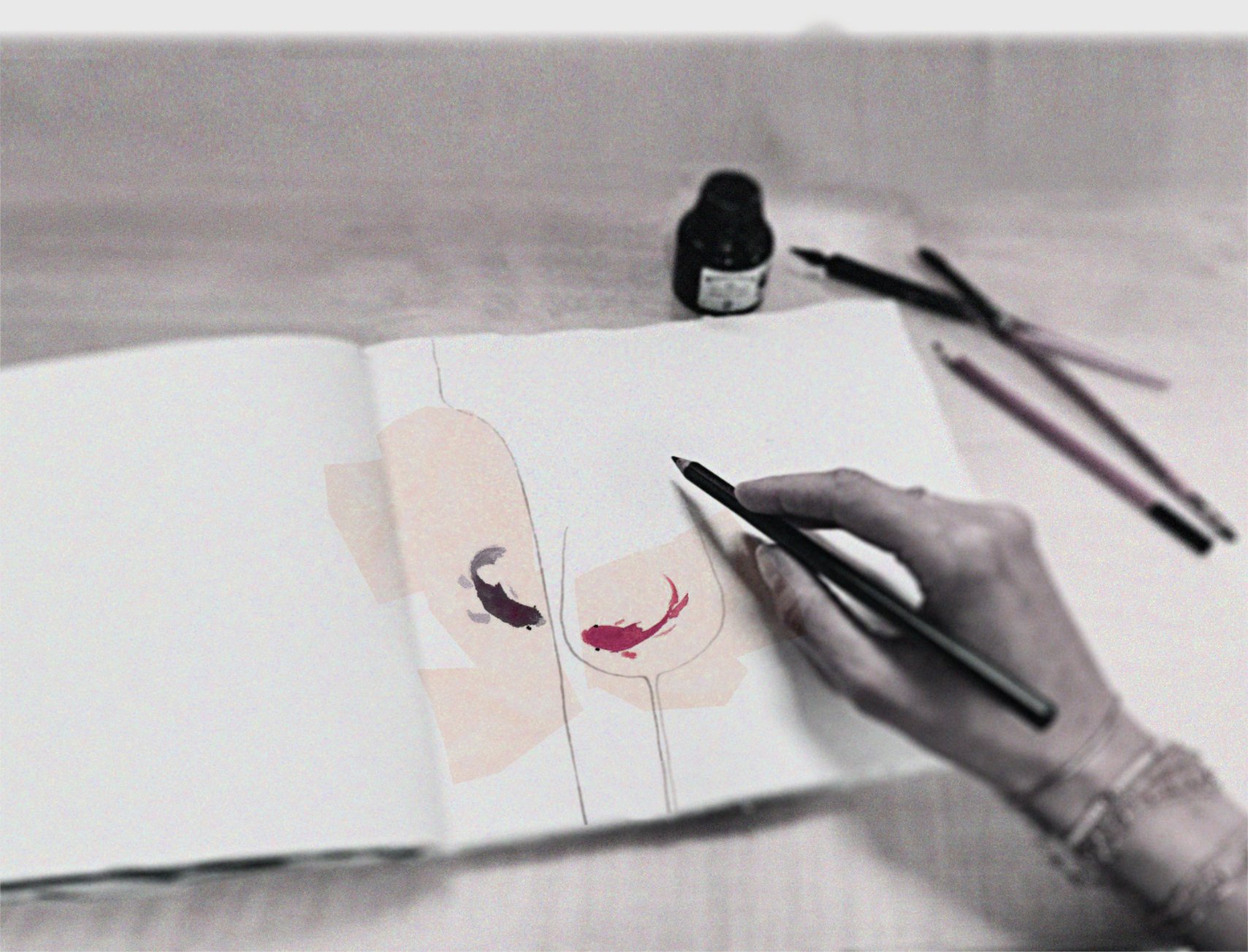 A person is painting abstract watercolor portraits of faces in a sketchbook. The face on the left has a purple eye and the face on the right has a red nose. There are two paintbrushes and a black ink bottle on the table.
