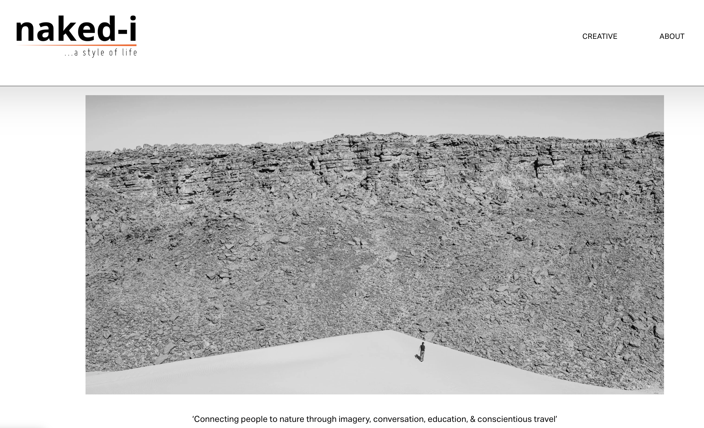 A black-and-white photograph of a rugged rocky landscape with a clear sky, featuring two small human figures walking on the terrain.