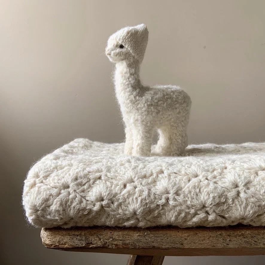 A white, plush, llama-shaped stuffed animal sitting on a fluffy, textured white surface.