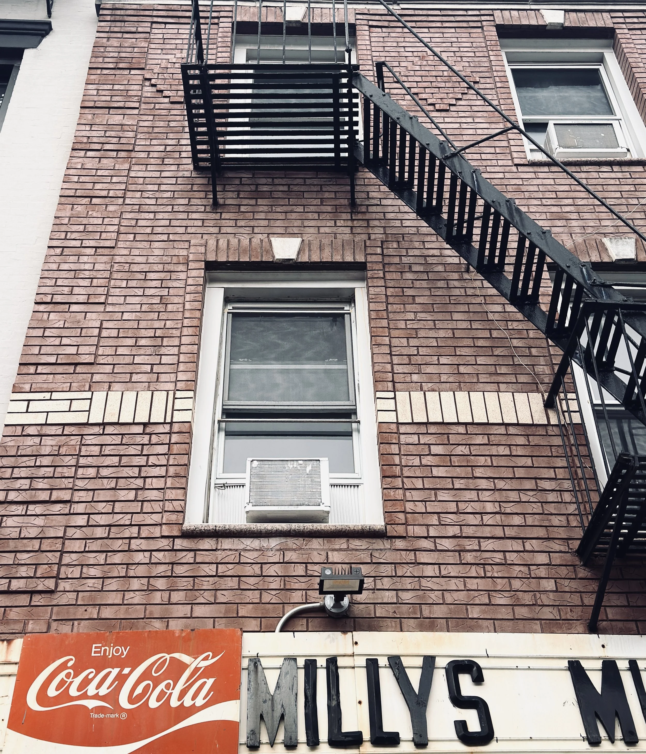 Red-brick building with black fire escape above a vintage Coca-Cola sign and Milly's shop sign, New York