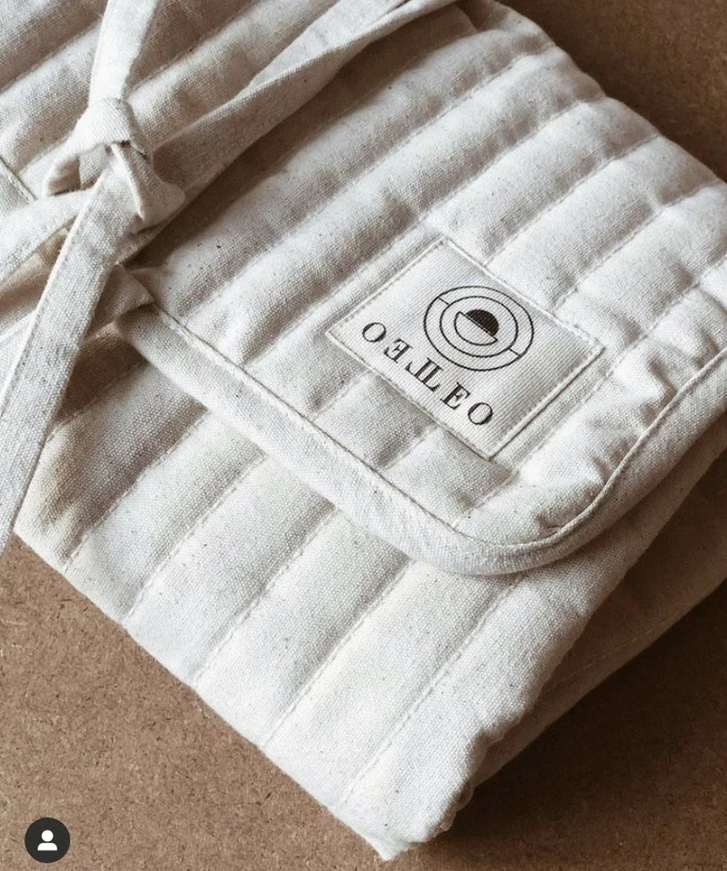 A folded pair of beige and white striped pants with a label reading "O BE IL EDO" and a circular logo, placed on a brown surface.
