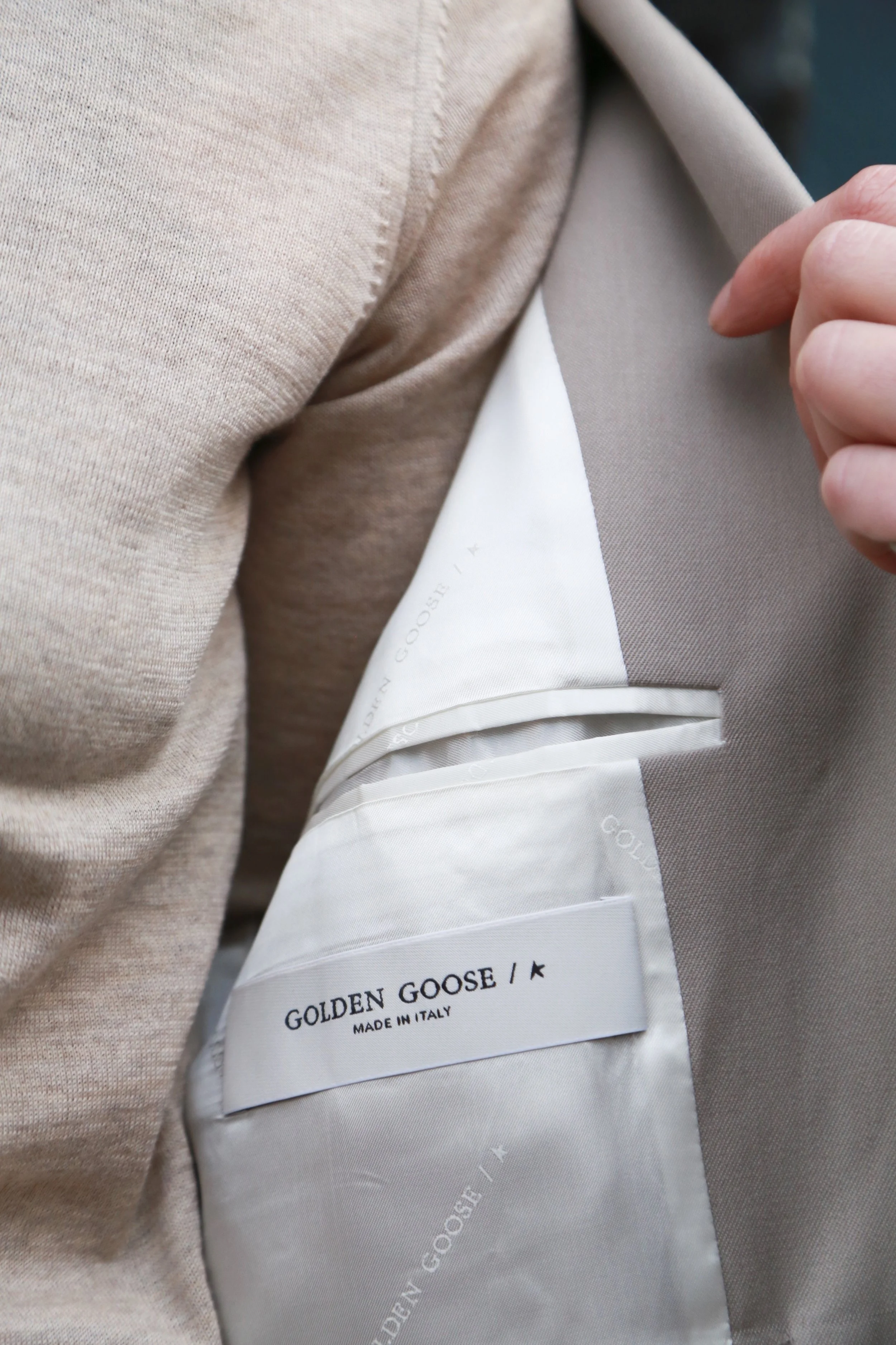 Close-up of a beige jacket's interior showing a white label that reads 'GOLDEN GOOSE / MADE IN ITALY'.