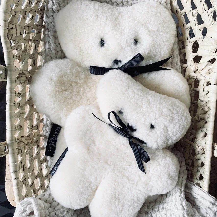 Two white plush teddy bears with black ribbons, sitting inside a woven wicker basket.