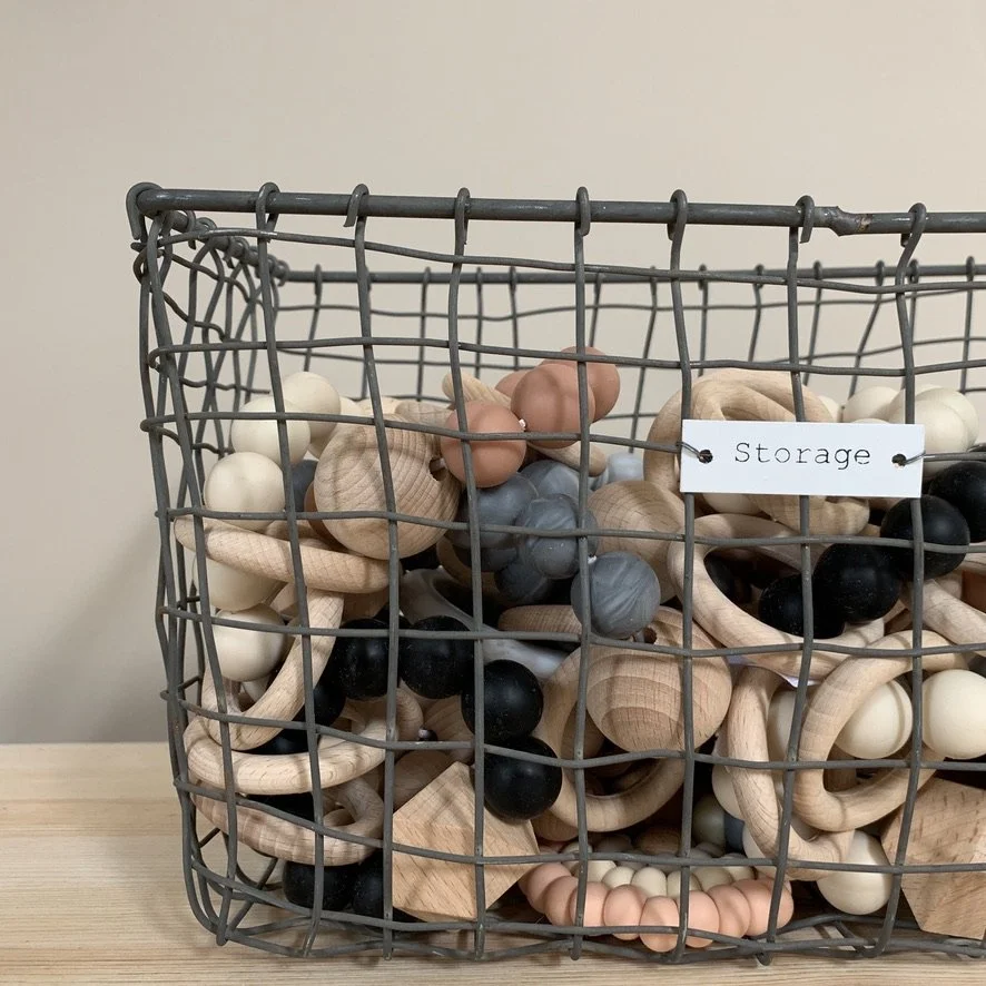 Wire basket filled with various wooden and silicone teething toys, labeled 'Storage' on a white sign.
