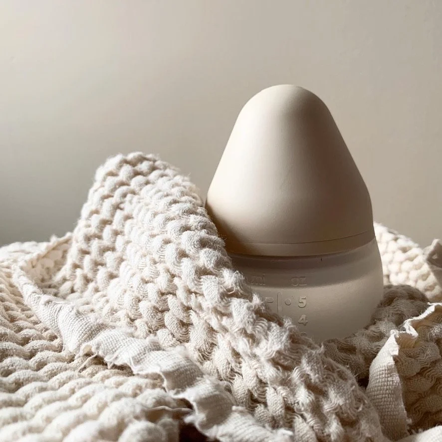 A white plastic humidifier or diffuser with a rounded top, placed on a textured, cream-colored blanket or fabric.