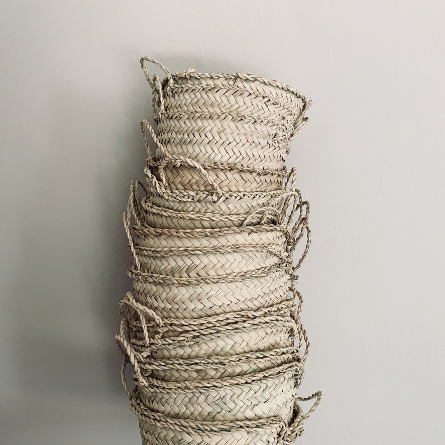 Stack of woven straw baskets tied with string against a plain white wall.