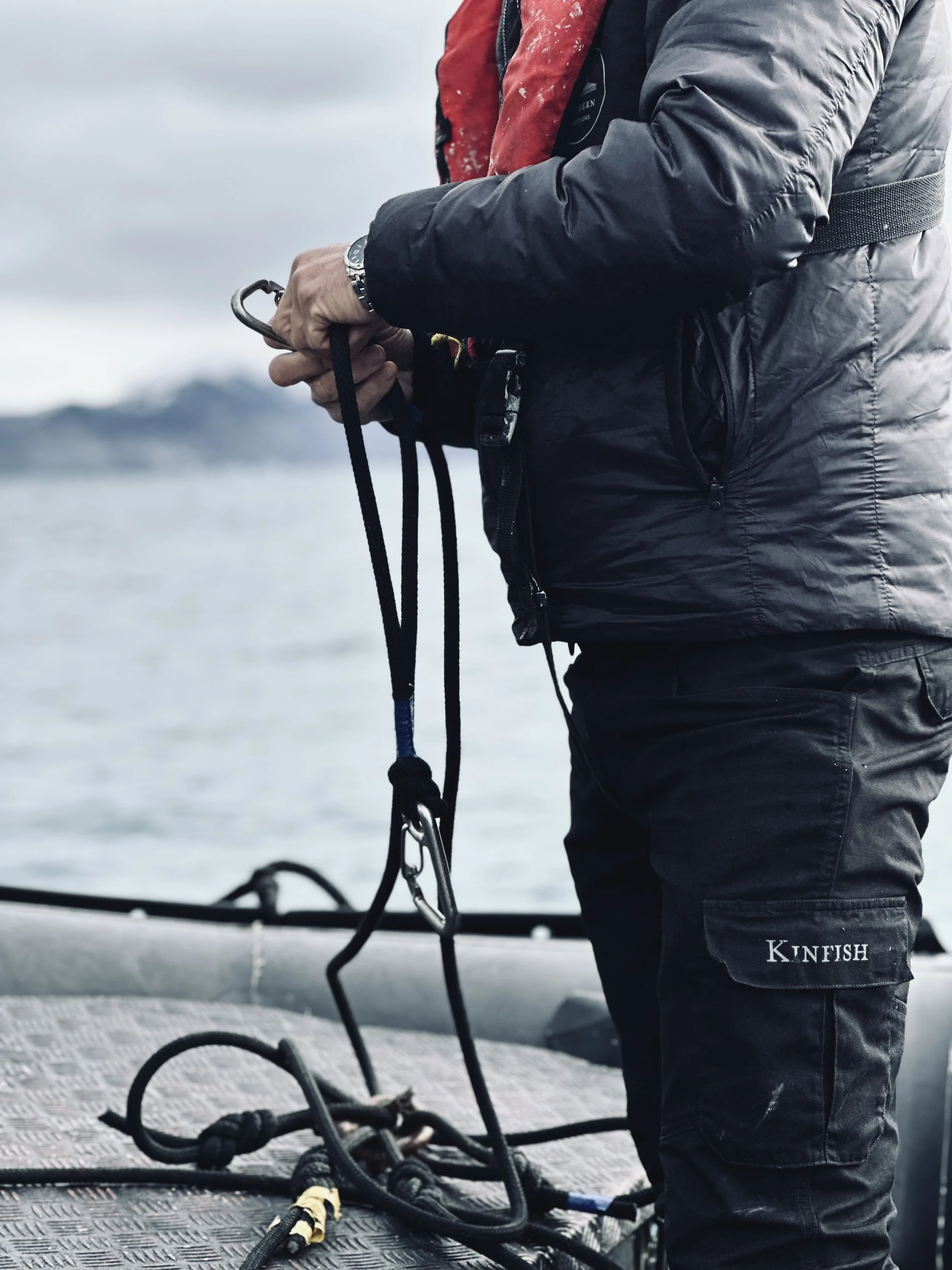 Person preparing fishing or boating gear on a boat with water and mountains in the background.