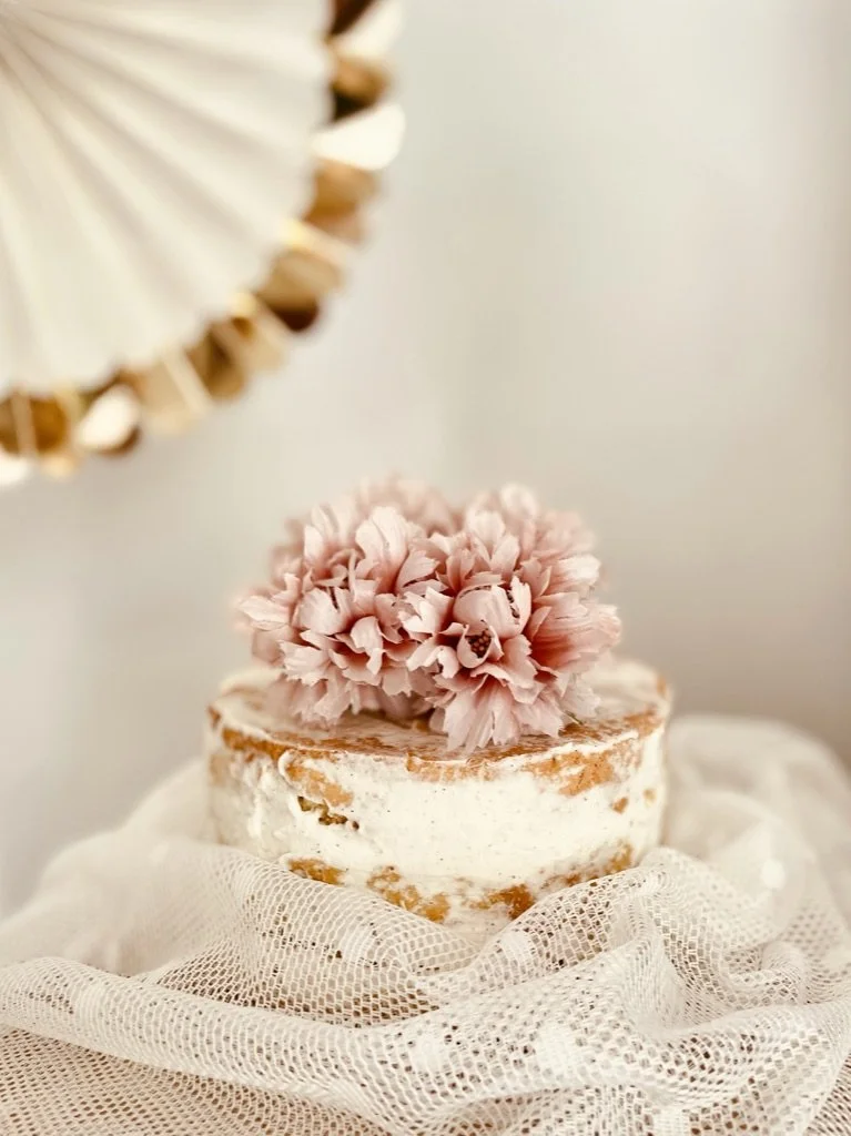 Dried pink flowers and decorated cake styled on neutral surface, editorial lifestyle photography by MUSE Creative Studio Brighton