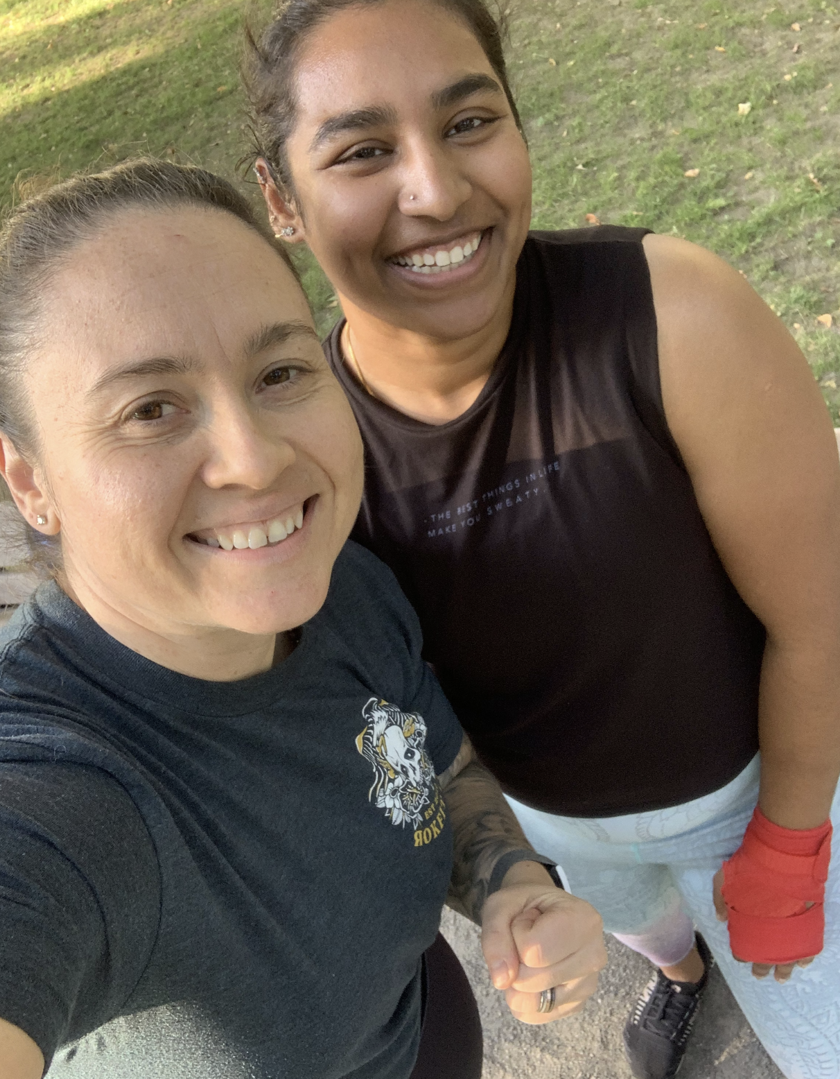 Two women taking a selfie outdoors on a grassy area, smiling at the camera.