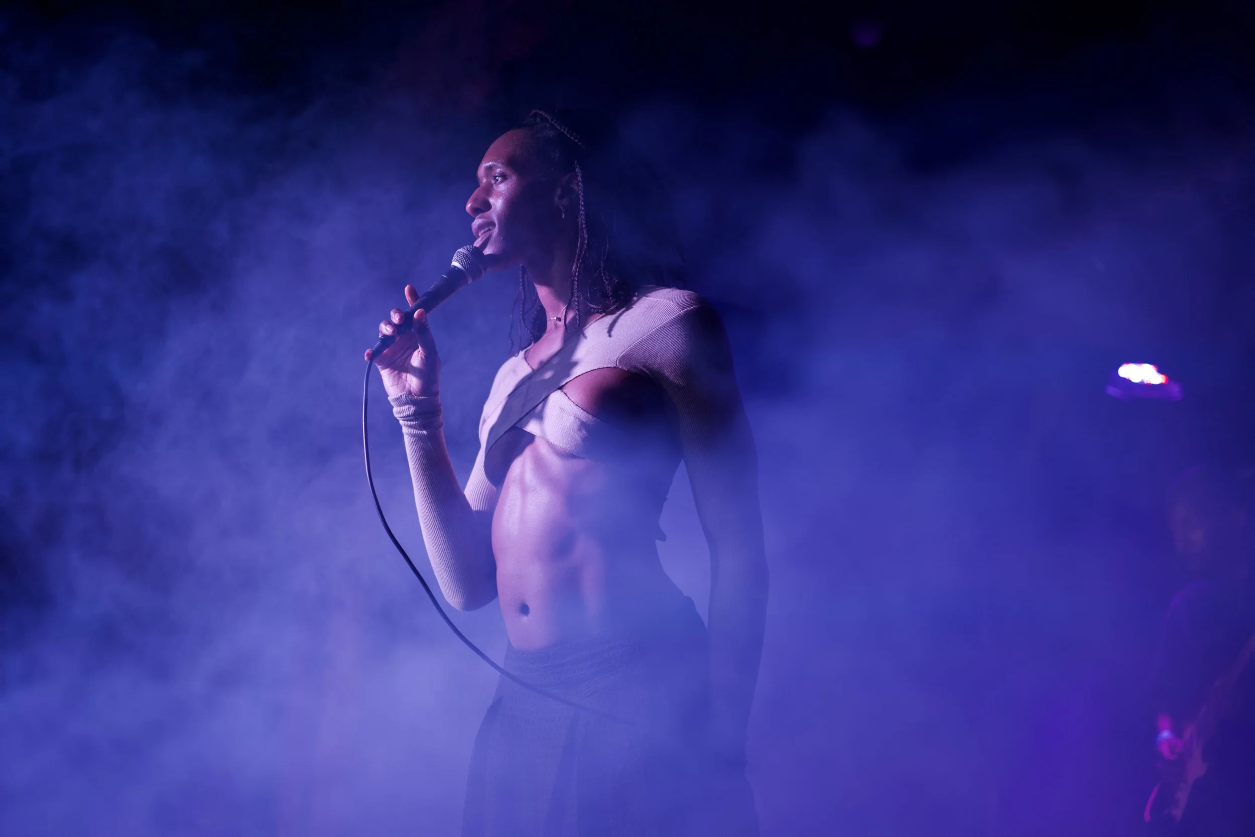 A woman holding a microphone appears to be performing on stage with purple and blue lighting and fog.