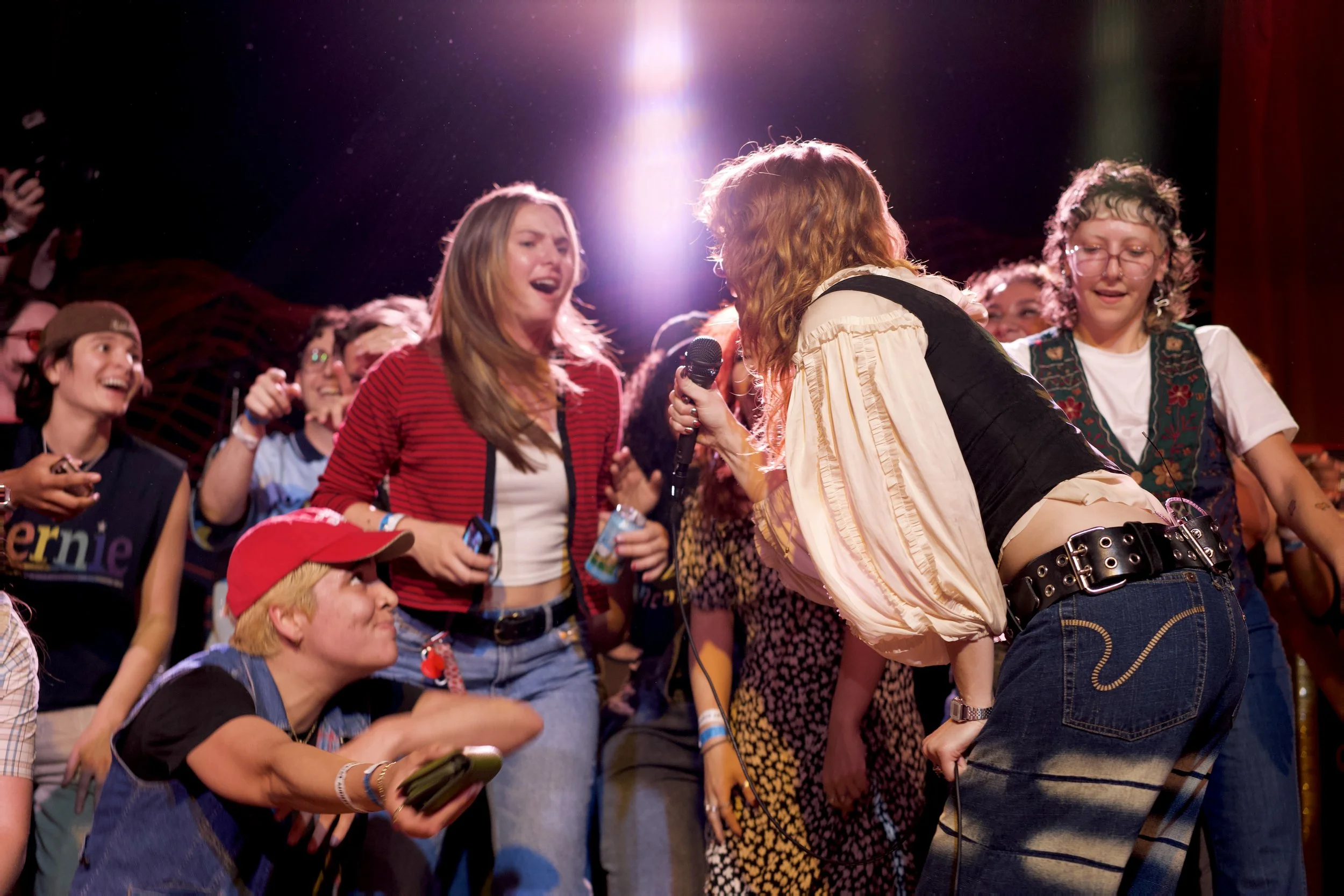 Group of people at an event, with some laughing and one person holding a microphone, illuminated by a bright light above.