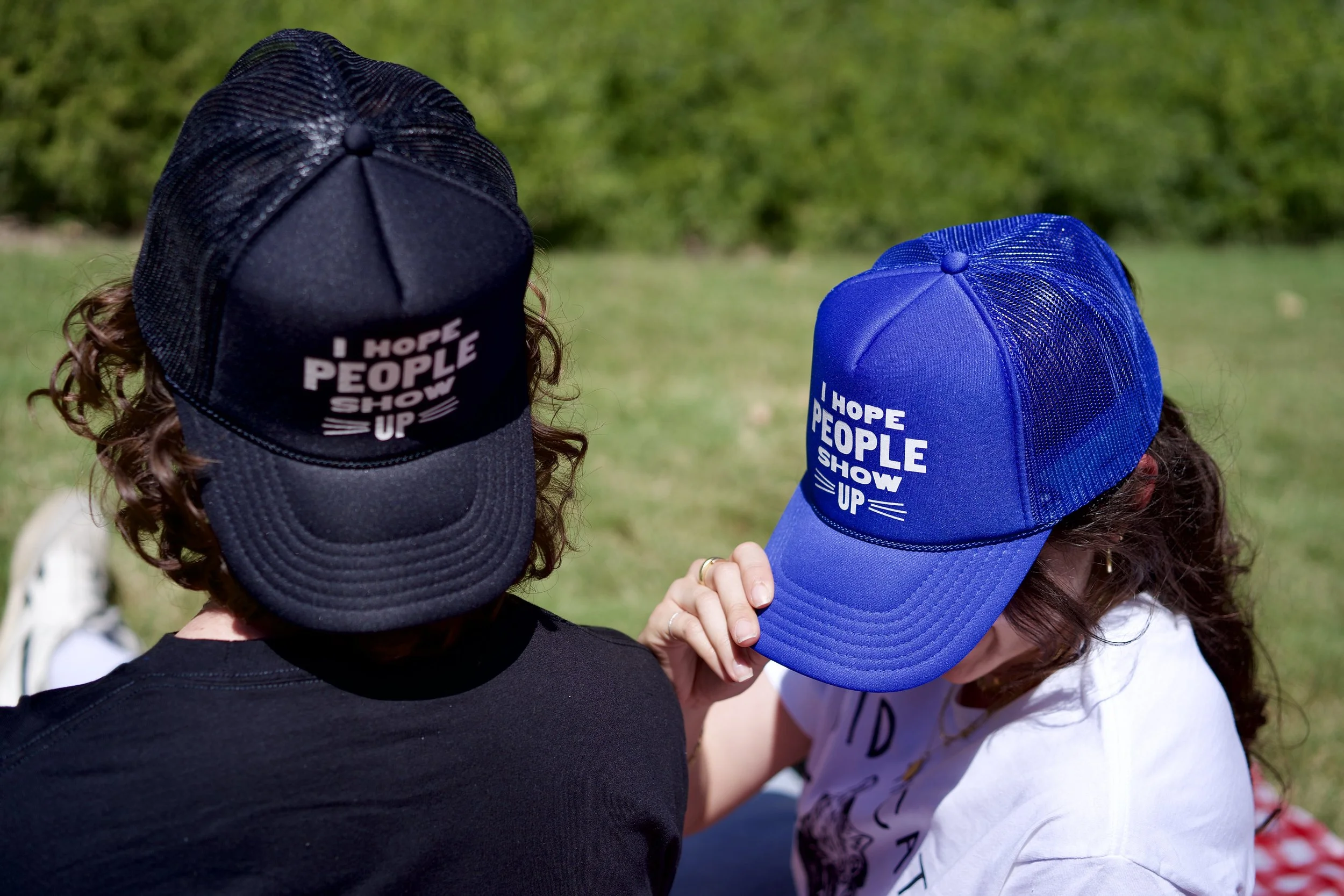 Two children with curly hair wearing black and blue baseball caps that say 'I hope people show up'.