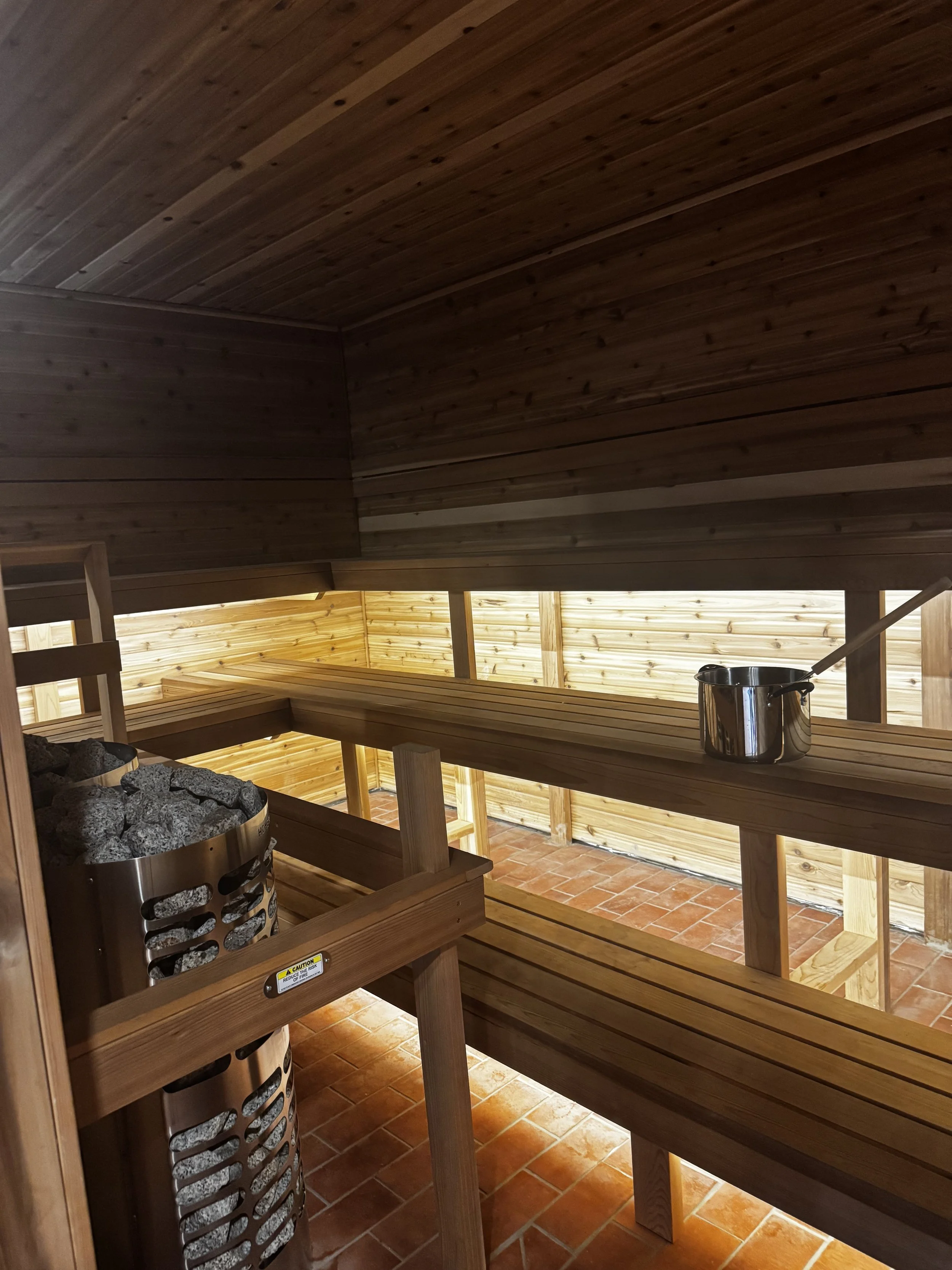 Wood-lined Finnish sauna with tiered cedar benches and a stone heater at Gainesville Sauna House