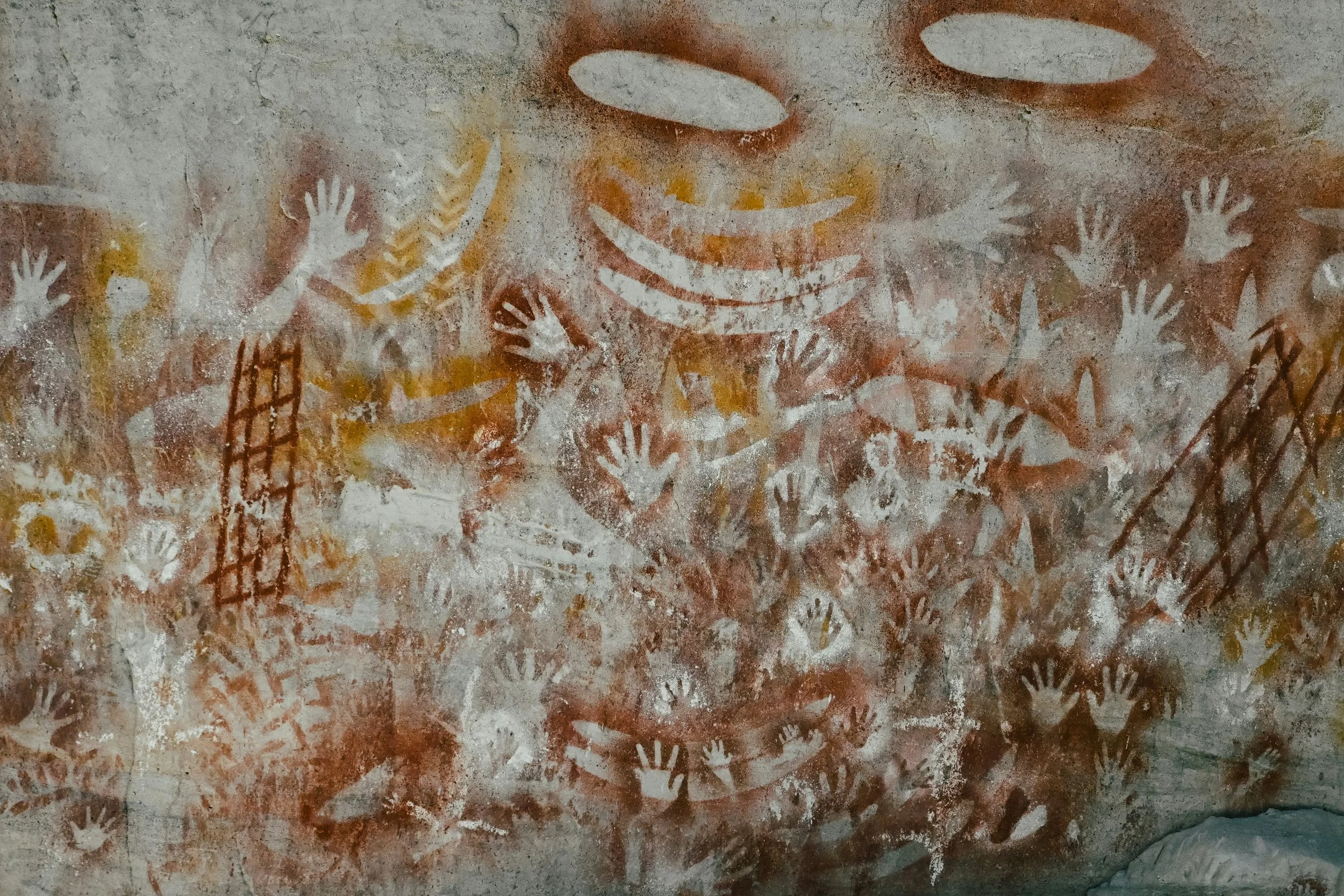 Ancient Aboriginal hand stencils in red and ochre pigment on a cave wall, representing human ancestry, deep history, and our inherited biology.