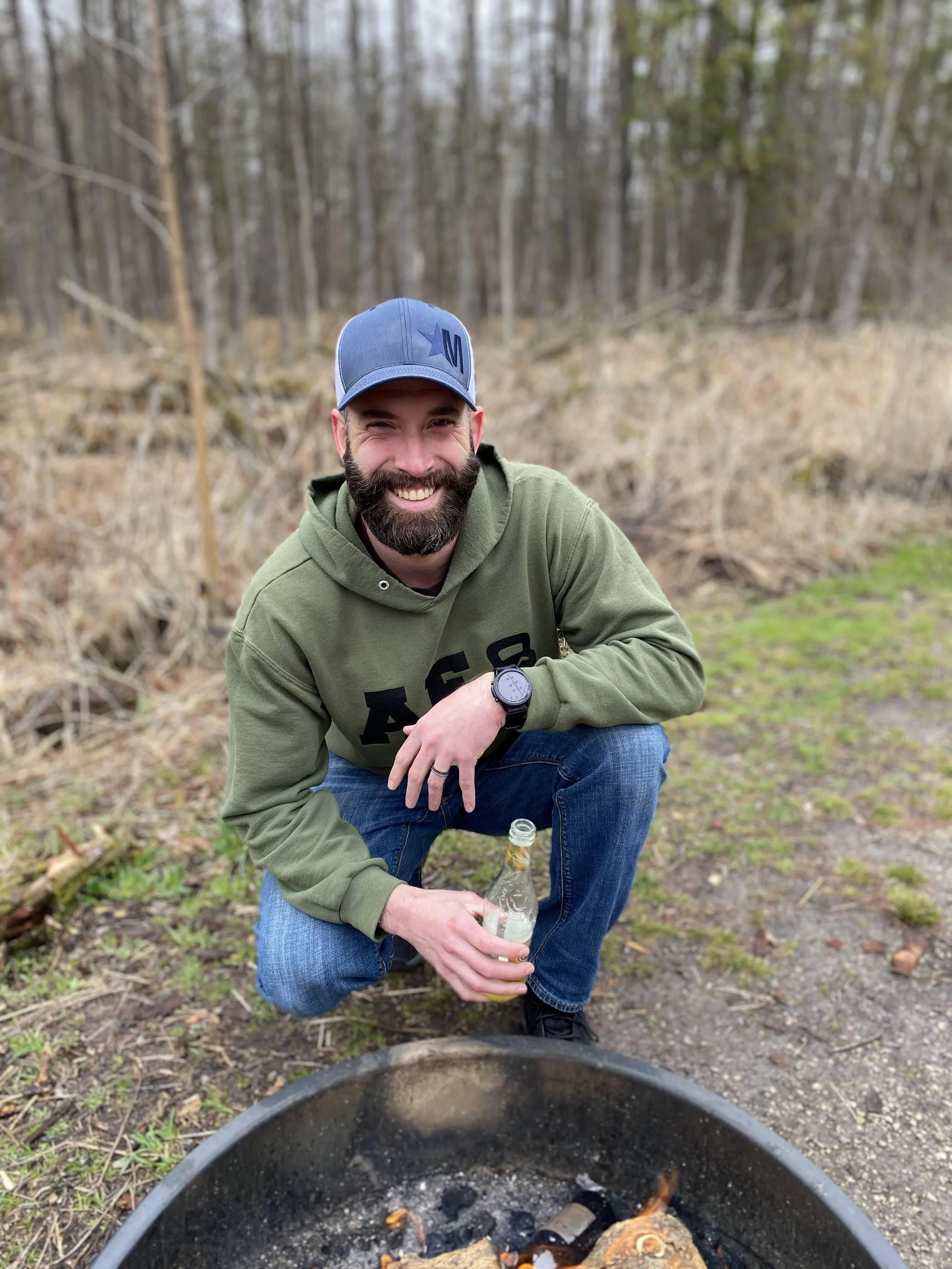 Health coach Brett Thomas smiling by a campfire, practicing ancestral living and outdoor recovery strategies.