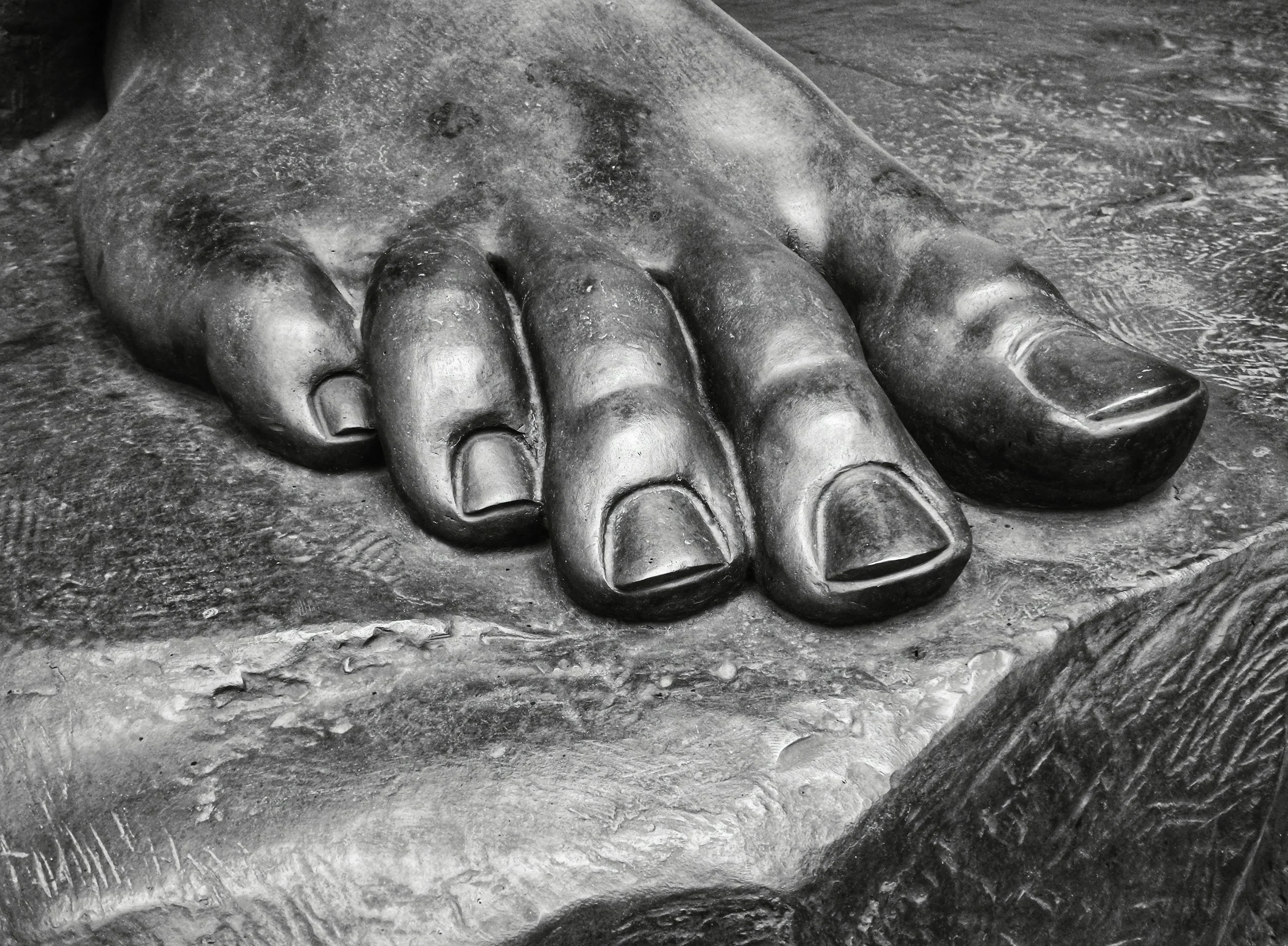 Black and white close-up of a stone statue's bare foot, showcasing the wide toe splay and natural structural alignment of the human foot.