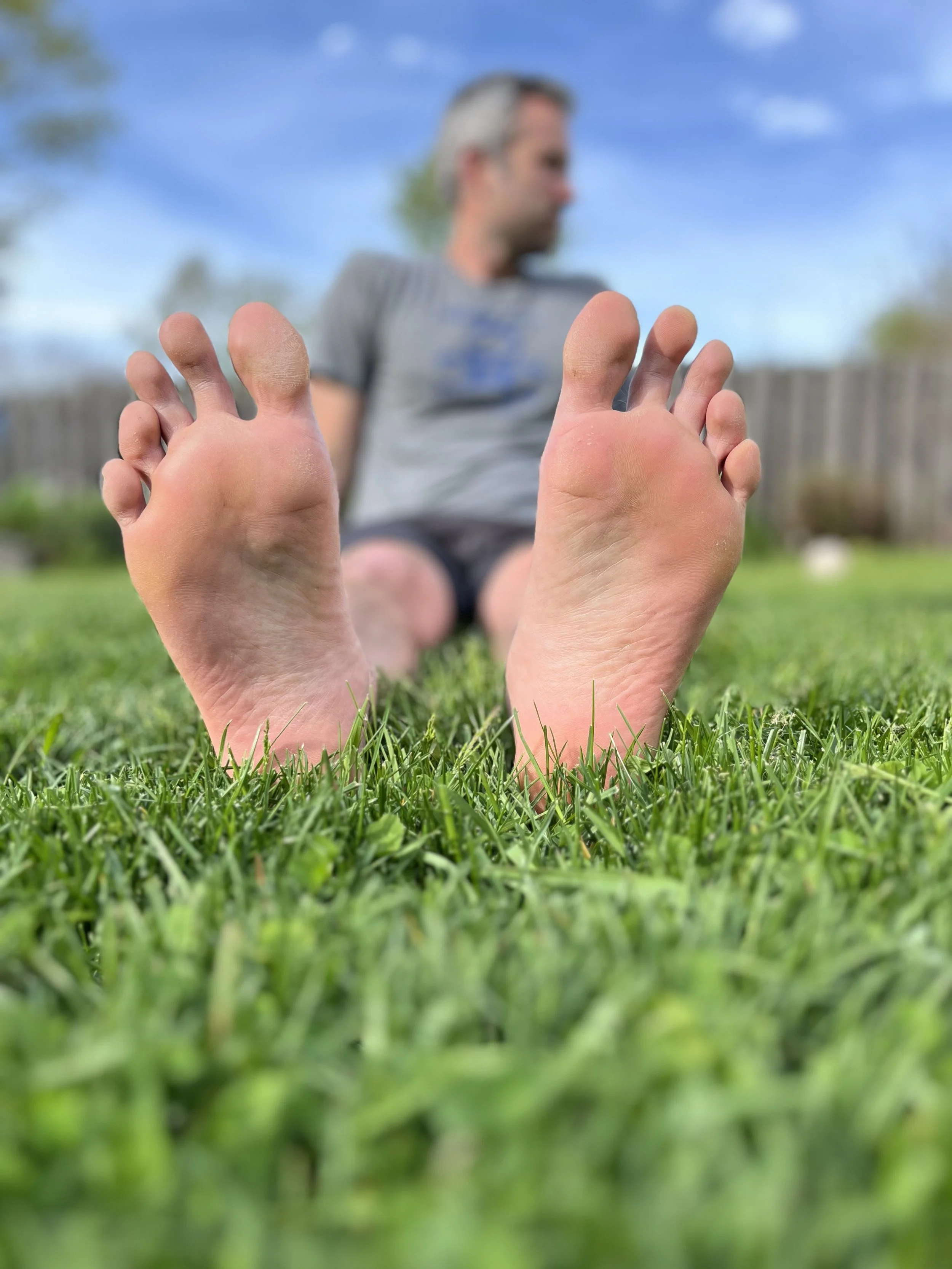Health coach showing bare feet resting on vibrant green grass, highlighting natural foot health and barefoot movement