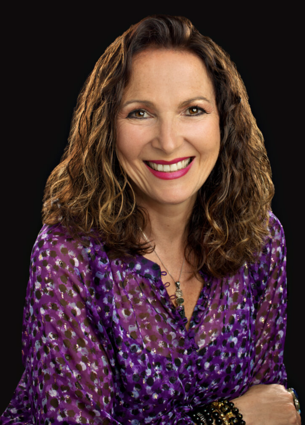 Claudia Rickard - creator of The Bunny Talk Process - A woman with curly brown hair smiling, wearing a purple patterned blouse, against a black background.