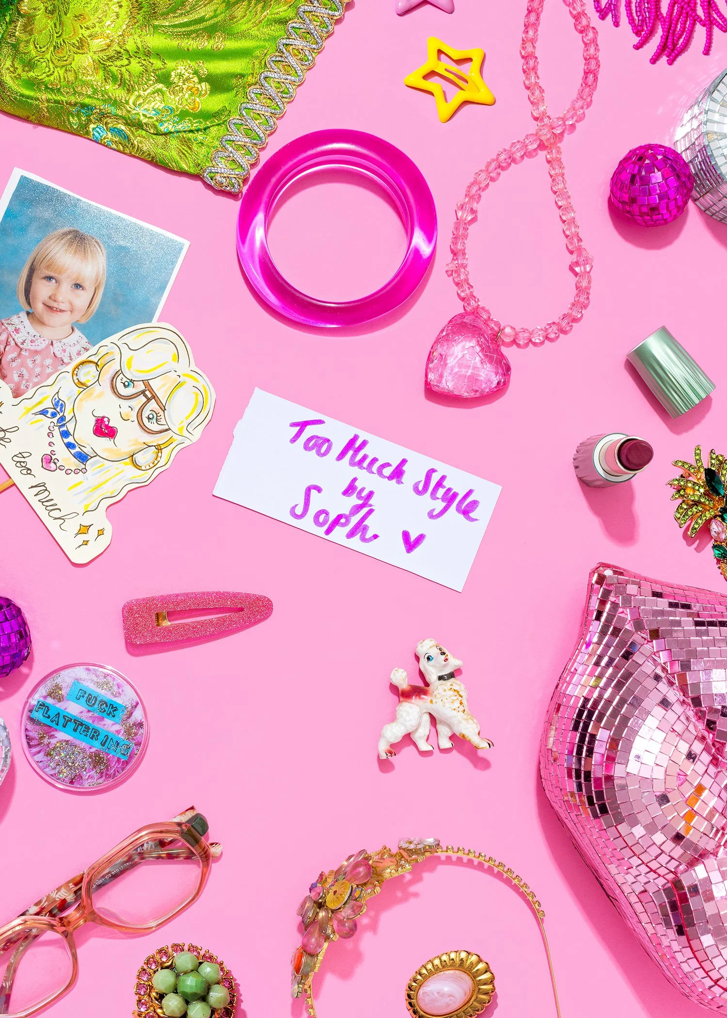 Various colorful fashion accessories and decorations arranged on a pink background, including jewelry, a photo of a young girl, a note, and decorative items such as a disco ball and a pink rhinestone clutch.