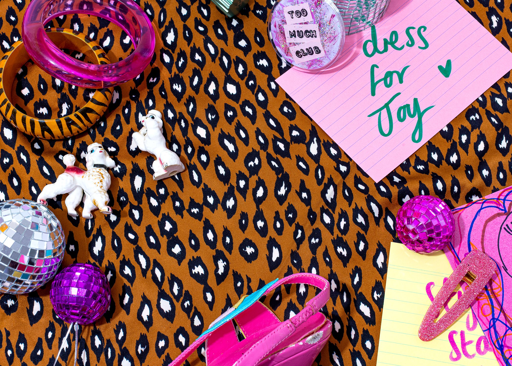 A colorful party setup with leopard print tablecloth, pink and purple accessories, small unicorn figurines, disco balls, and a pink note that says "dress for joy" with a heart.
