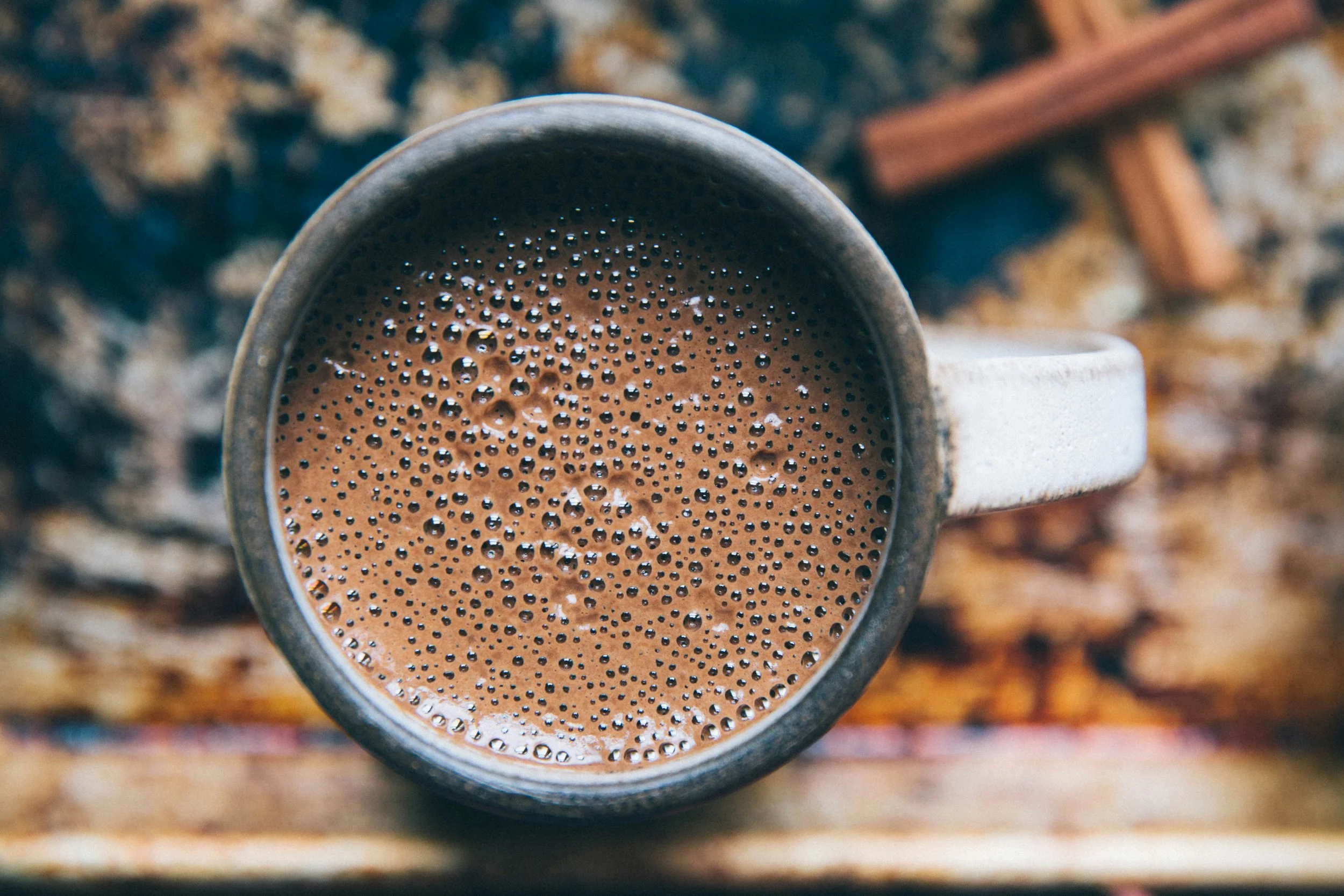 Große Tasse mit Kakao, daneben Zimtstangen, Blick von oben.