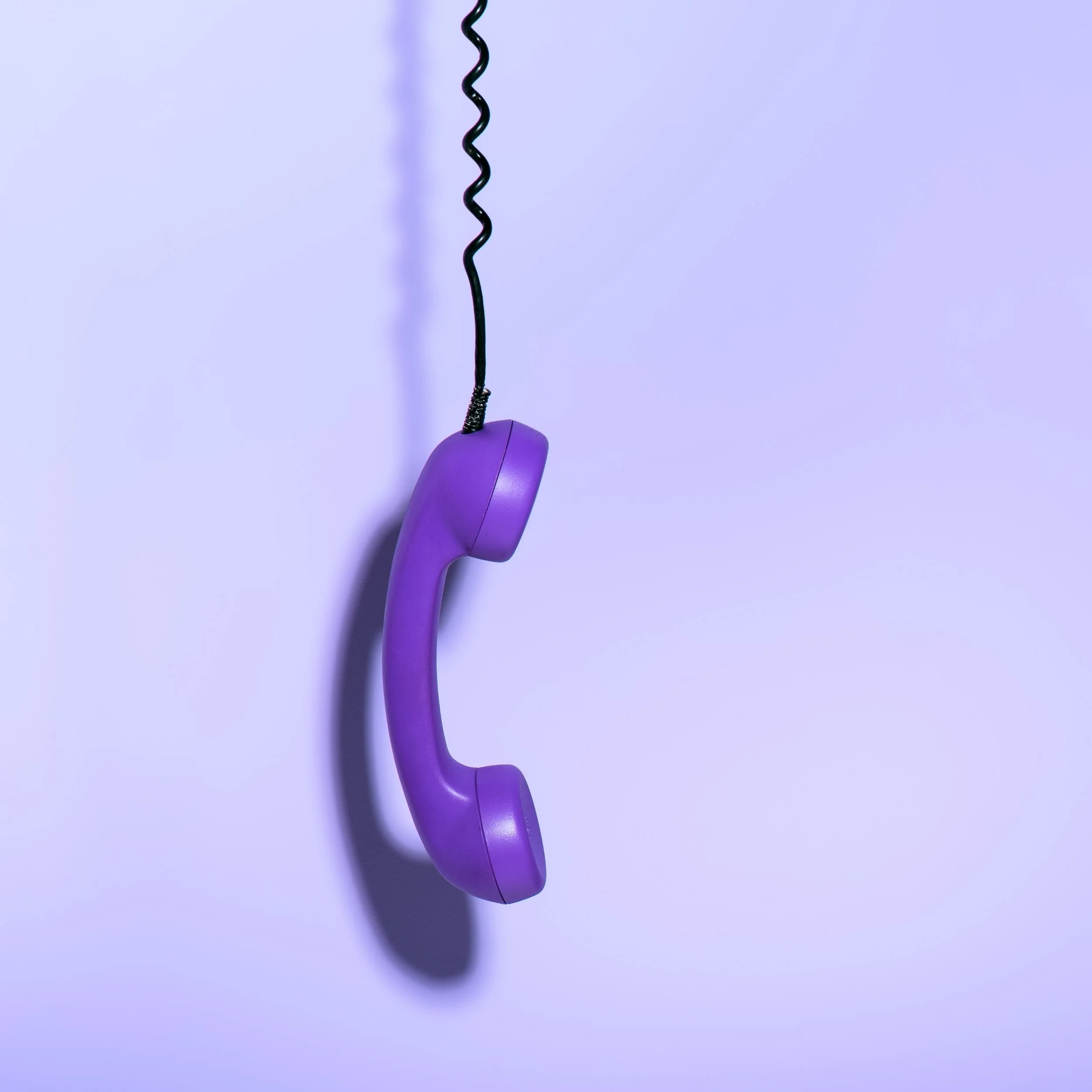 A purple phone receiver hangs down suspended by its cord against a lighter purple background