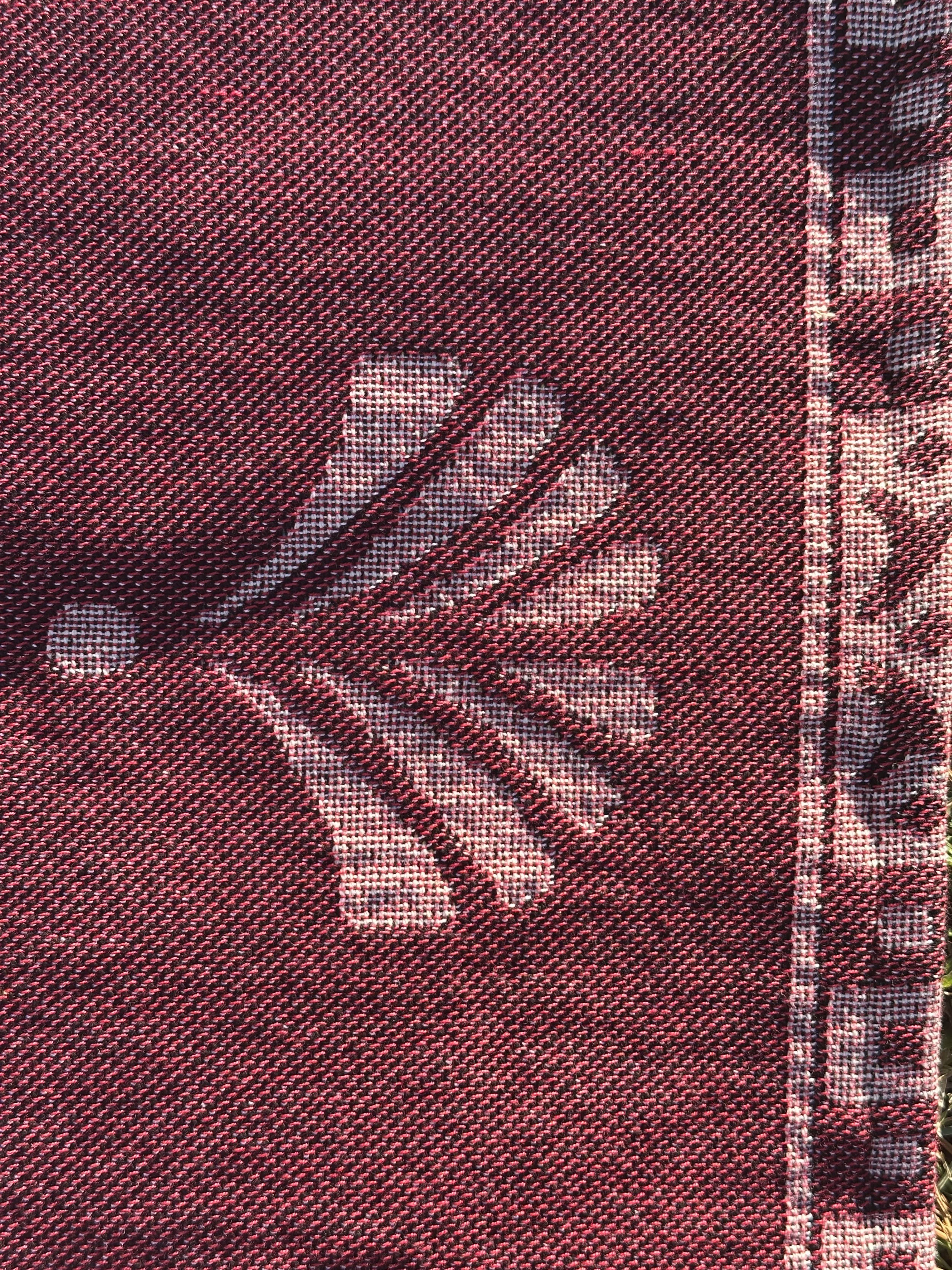 This image shows a detail shot of the tassel decoration and the ornamental border on the top of the blanket, showing more of the squares and historical or vintage style decoration