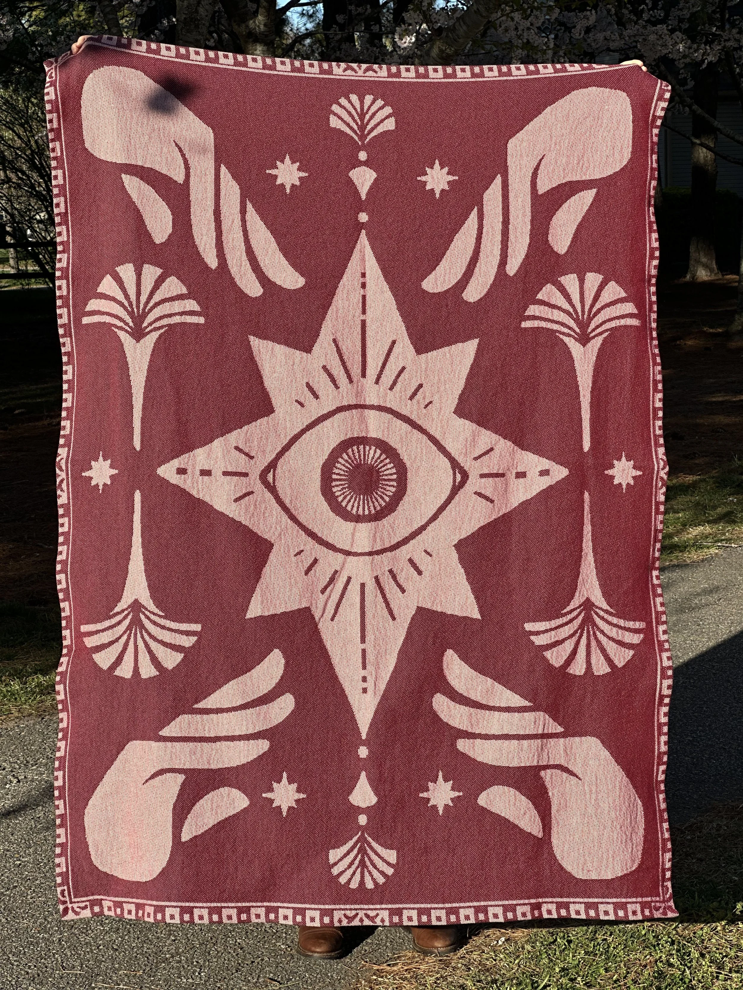 Mauve and pale pink woven tapestry blanket featuring symetrical esoteric art, reaching hands, starbursts and other celestial imagery, Art Deco style palms and tassels, and a vintage decorative border