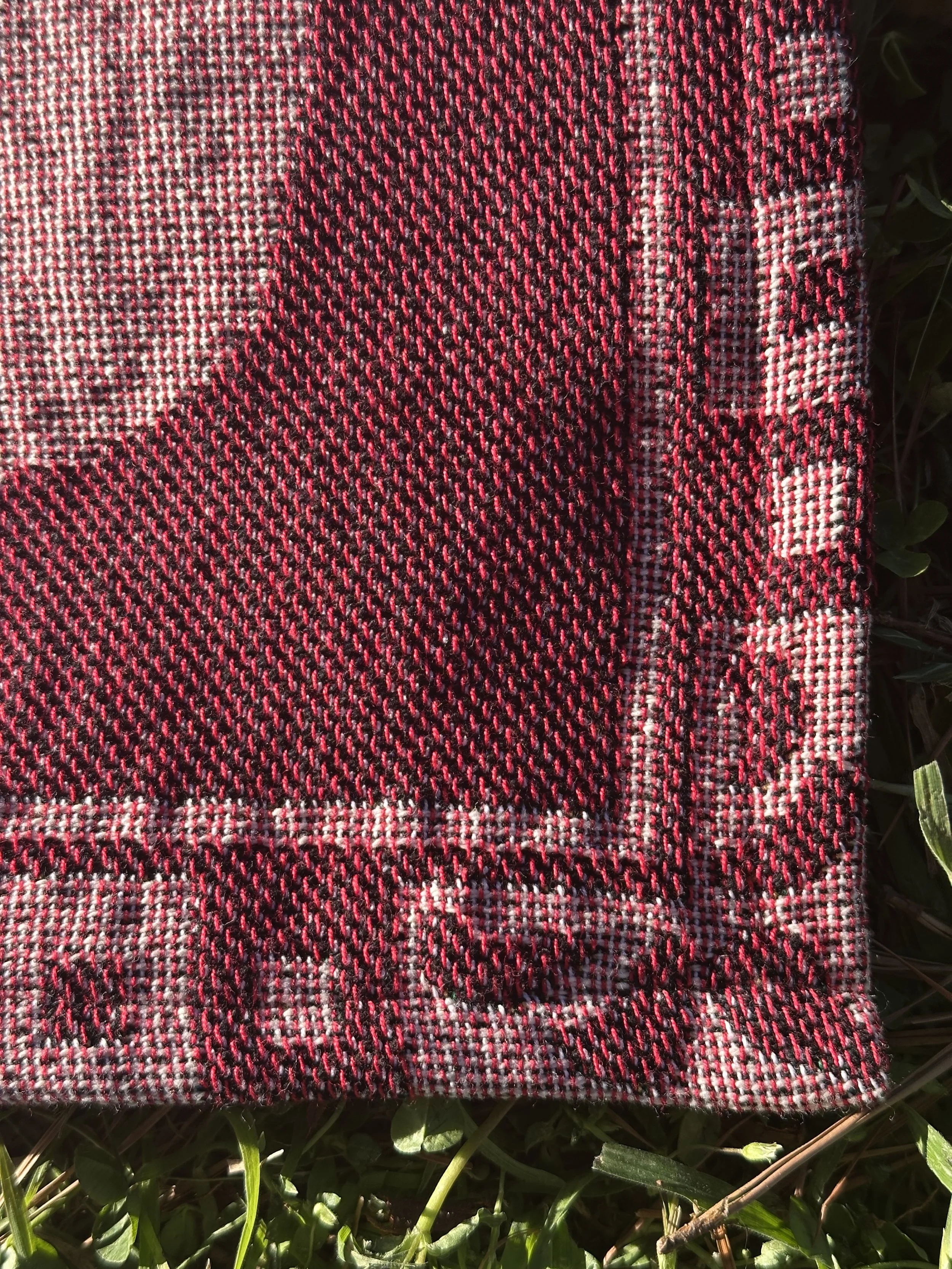 A close up detail shot of the corner of the blanket, showing the symmetrical border of squares in alternating colors as well as ornamental filligree that looks like a fountain or a blooming flower