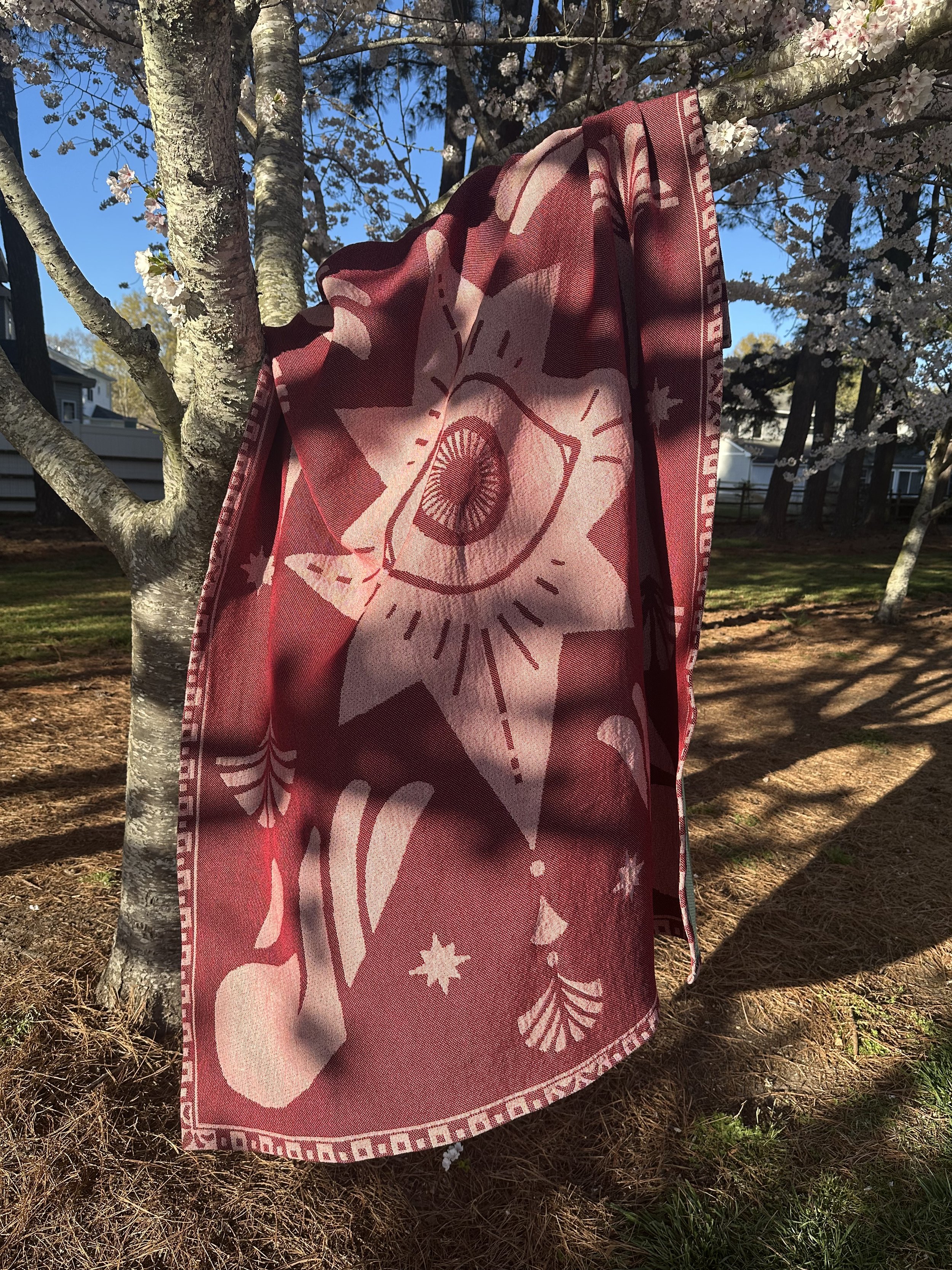 This image shows the blanket whimsically thrown over the branch of a cherry tree. It feels breezy and cozy