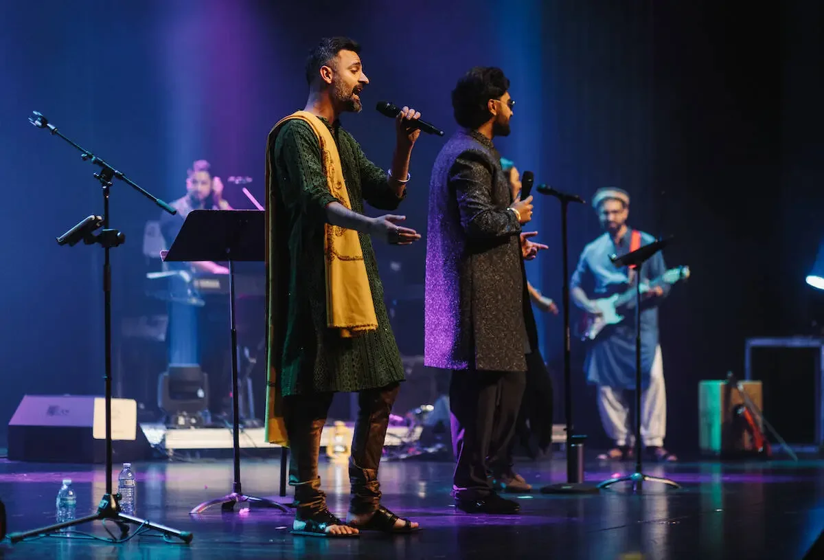 Group of musicians performing on stage with microphones and musical instruments, under colorful stage lighting.