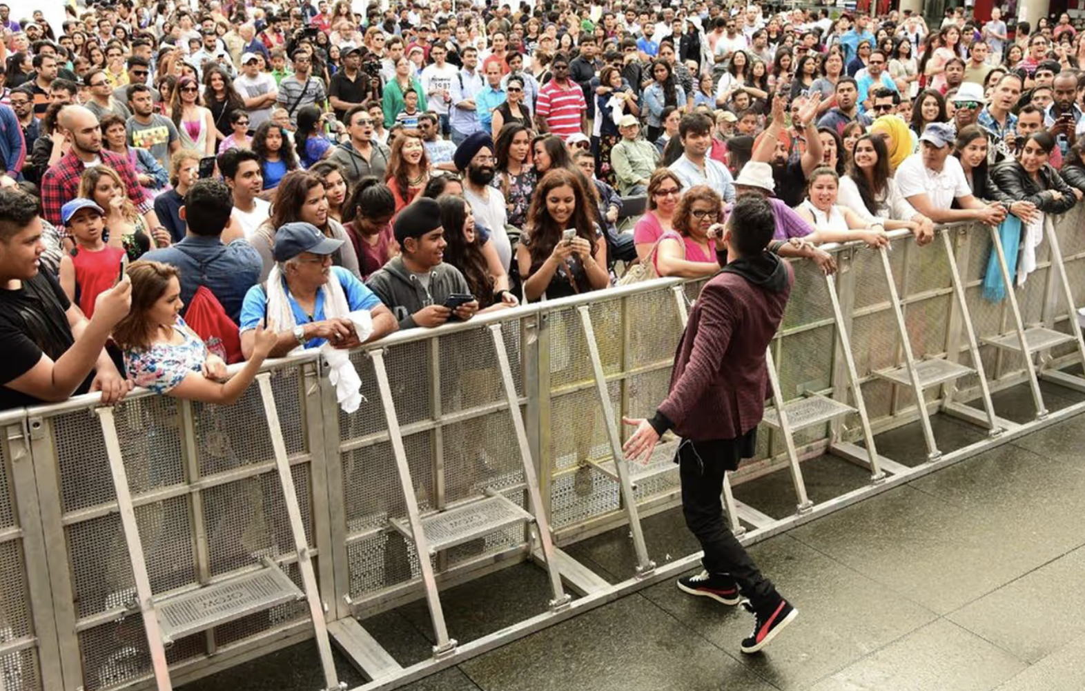 A man on a stage engaging with a large, diverse audience behind a barricade at an outdoor event.