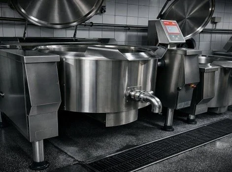 Large stainless steel industrial fermentation or mixing tank with control panel in a commercial kitchen or brewery.