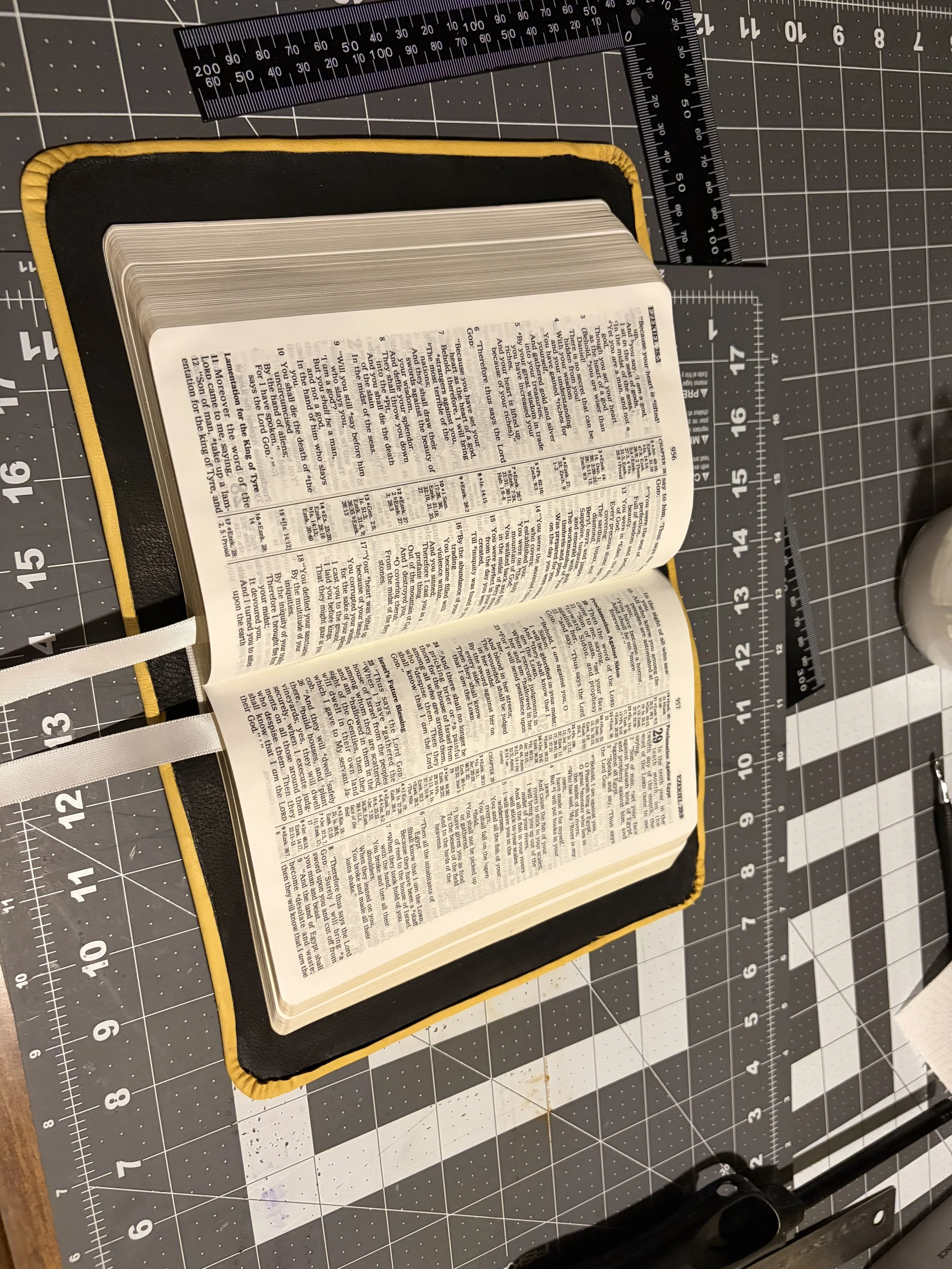 Open Bible placed on a yellow and black cover, set on a black all-purpose crafting mat with measurement guides and grid lines.