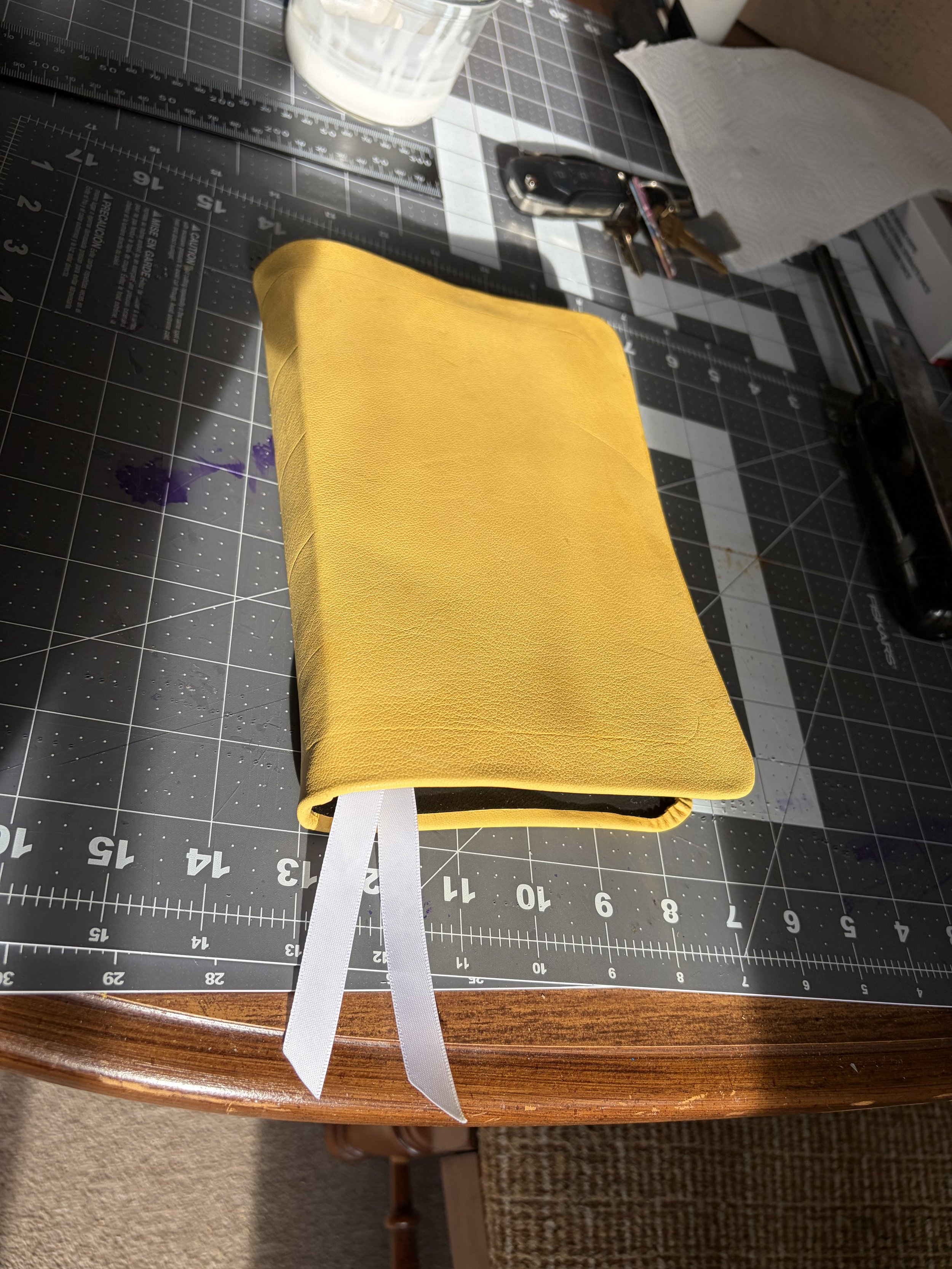 A yellow notebook with white ribbons on a worktable with cutting grid and tools.