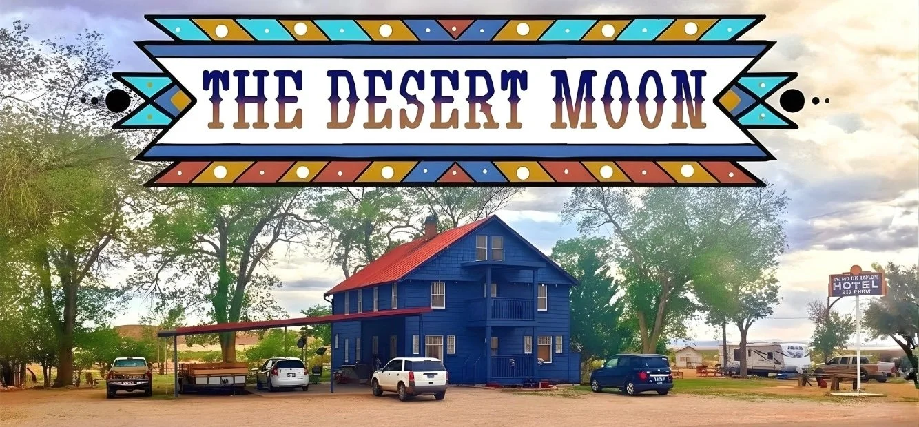 A sign with the words 'The Desert Moon' hangs above a blue building with a red roof. There are several cars parked in front of the building, and trees and a cloudy sky are visible in the background.