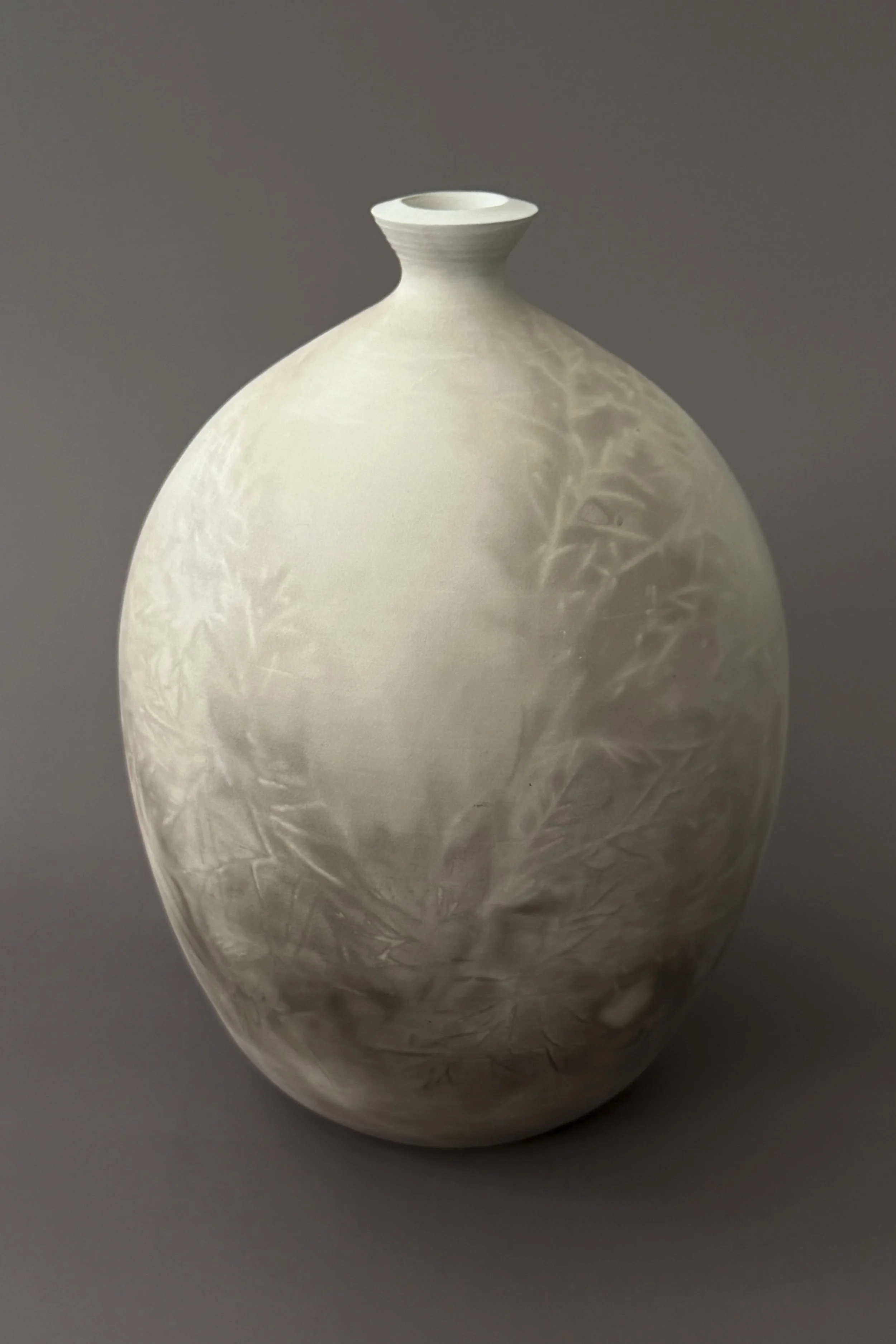 A white ceramic vase with a narrow opening and rounded body, featuring textured surface and subtle patterns.