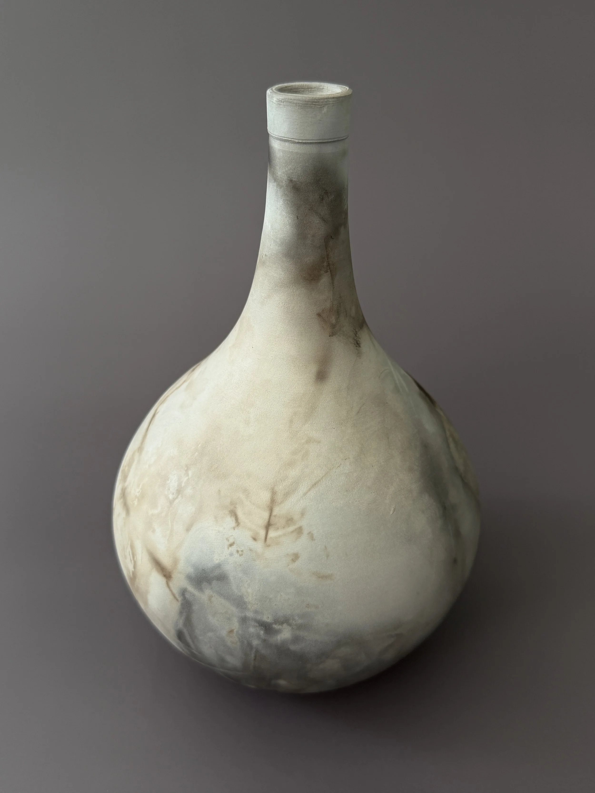 A pottery vase with a rounded base and a long narrow neck, decorated with a marbled pattern of light and dark earth tones.