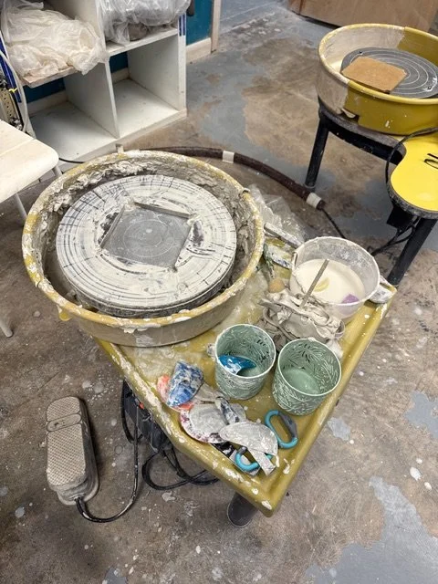 A pottery wheel surrounded by clay, tools, and ceramic bowls in a pottery studio.