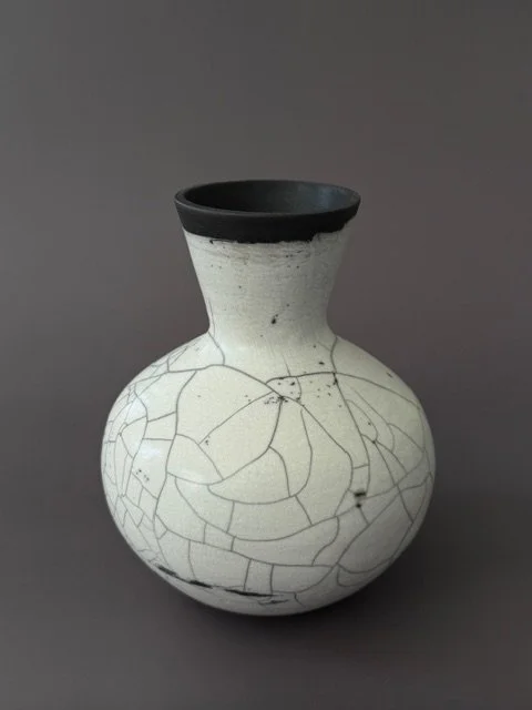 A white ceramic vase with black crackle patterns and a black rim on a gray background.