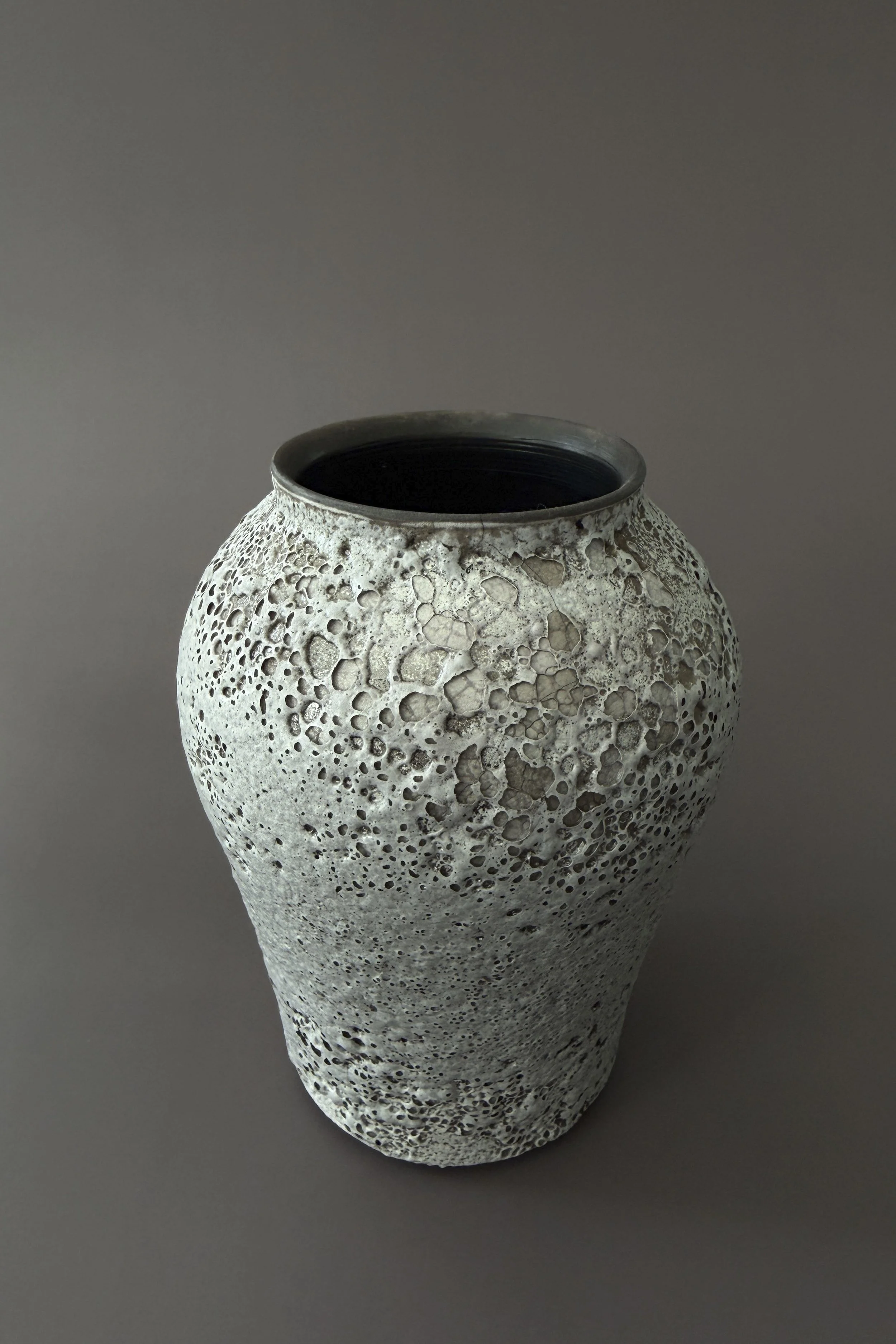 Decorative ceramic vase with a porous, textured surface and an open top, placed against a plain background.