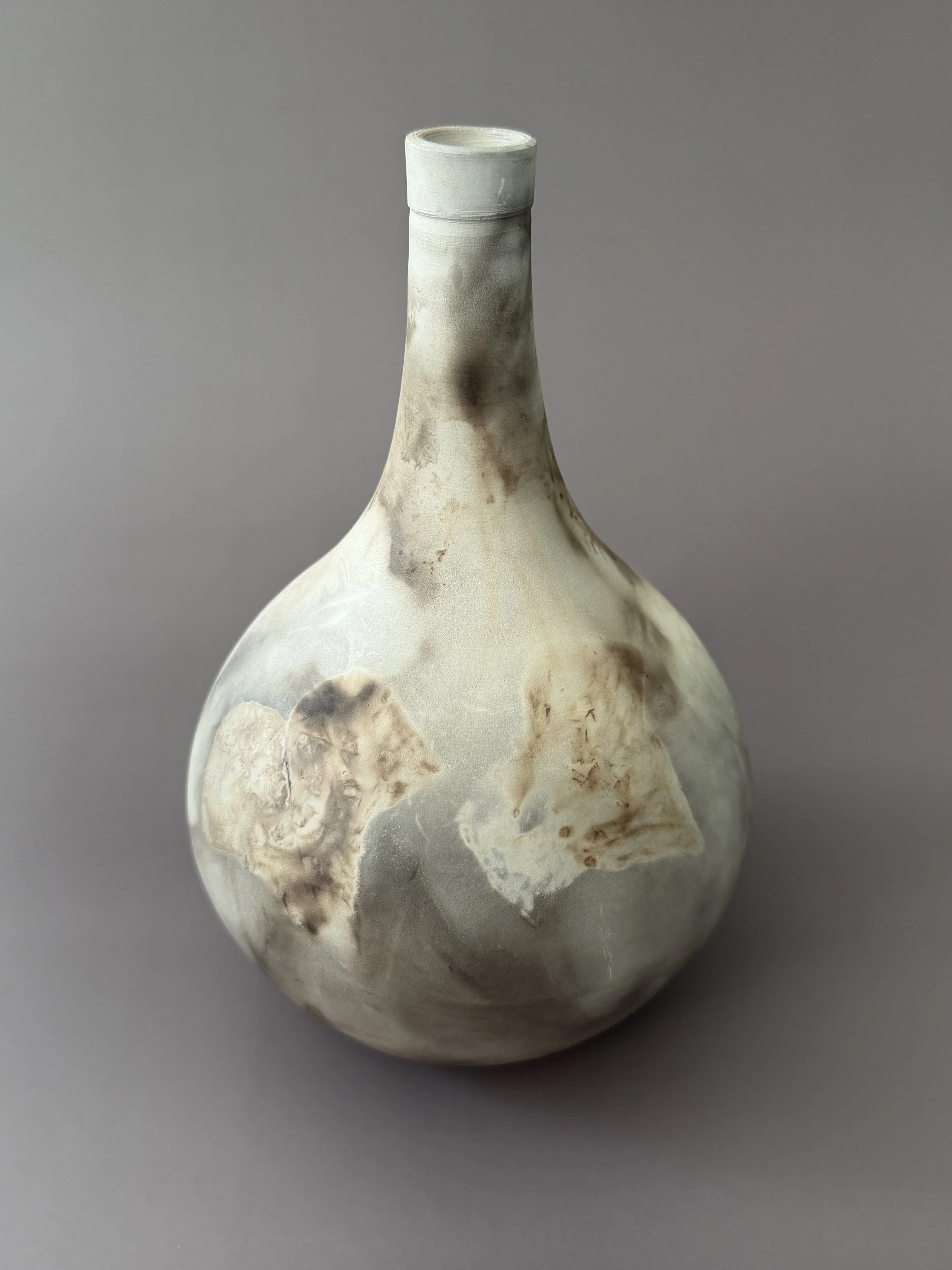 A ceramic vase with a rounded body and a long narrow neck, featuring a marbled pattern of whites, grays, and browns.