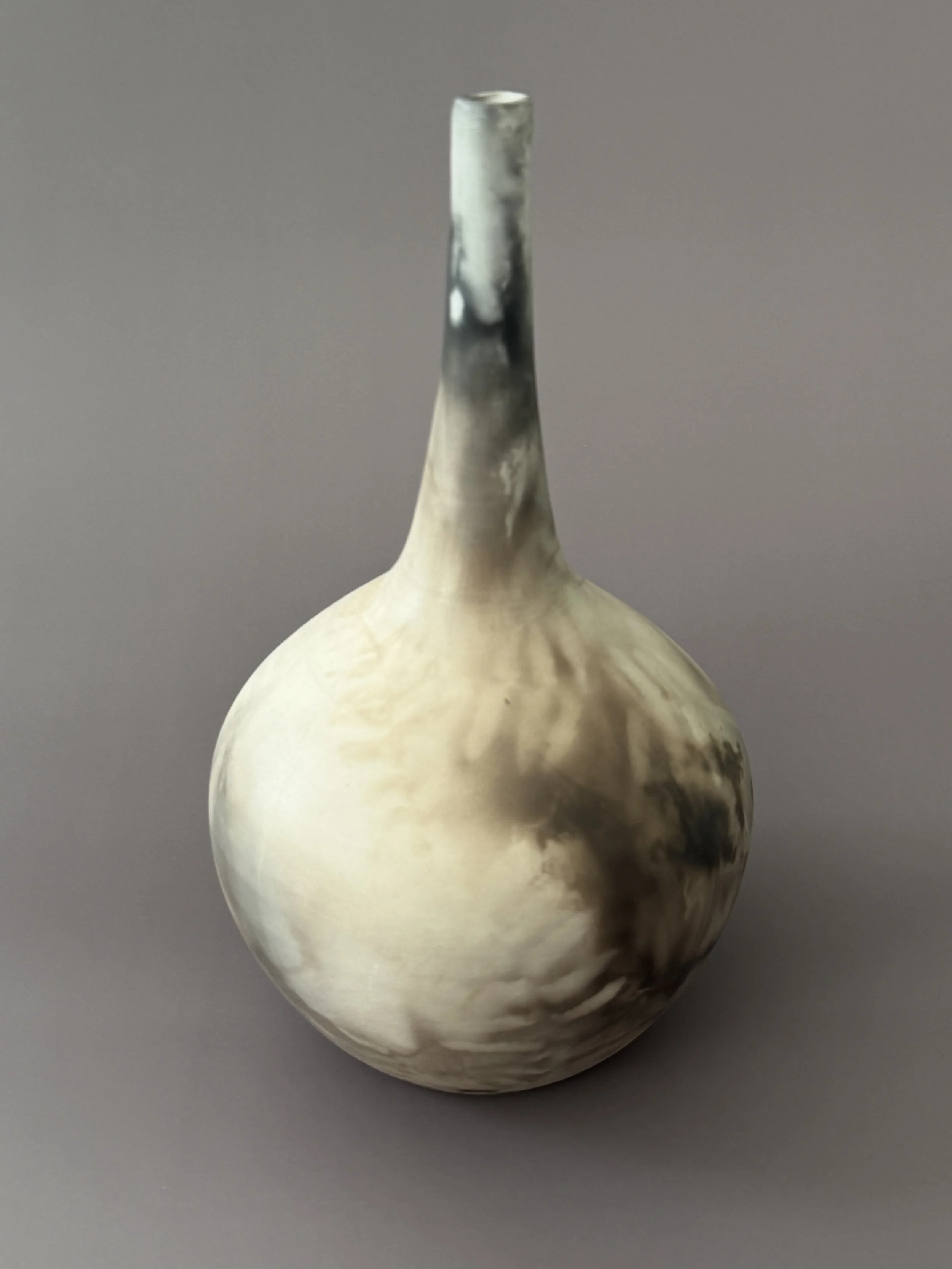 A ceramic vase with a wide rounded body and a long slender neck, featuring featuring a black and white pattern made by leaves and smoke.