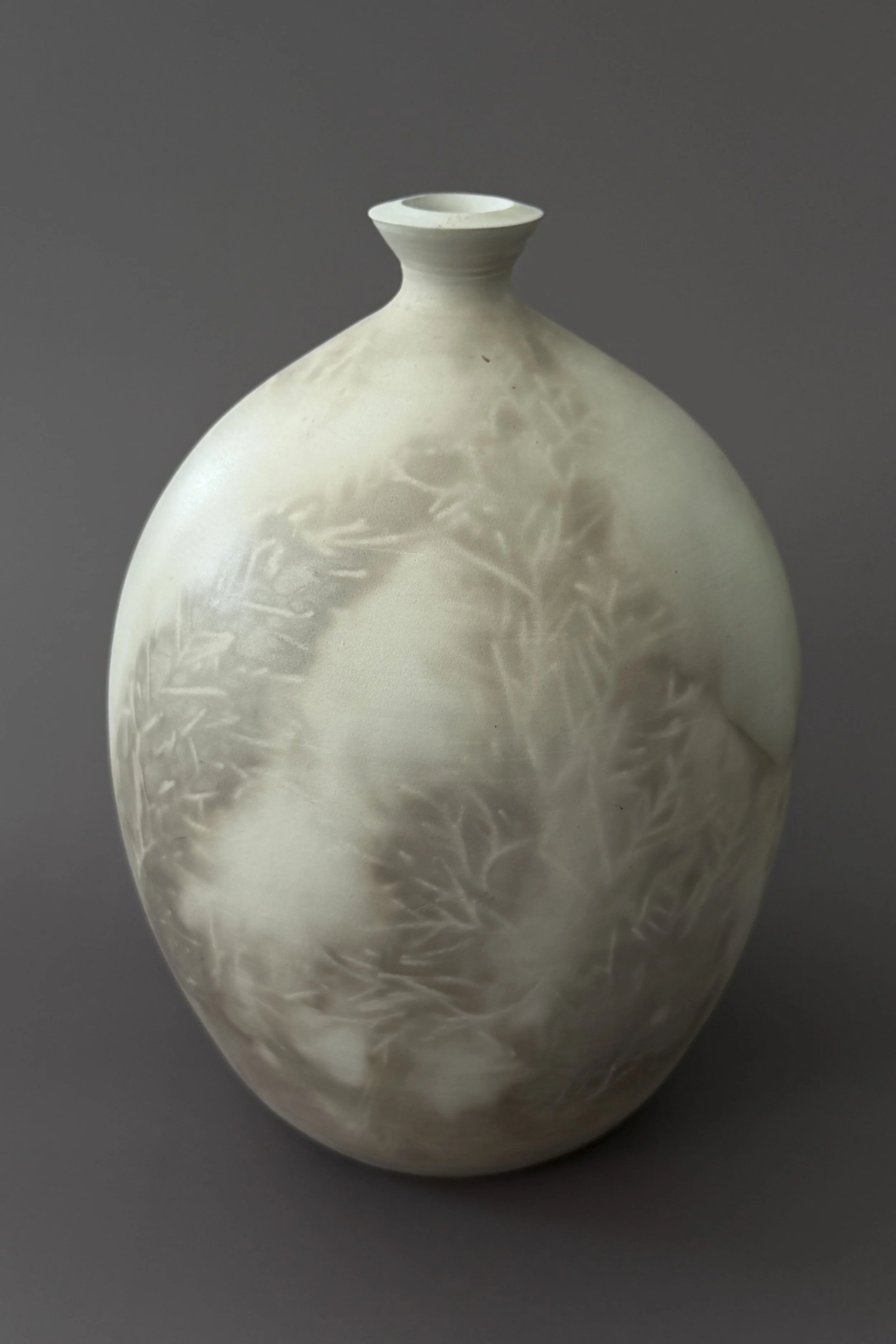 A white ceramic vase with etched leaf patterns on a gray background.